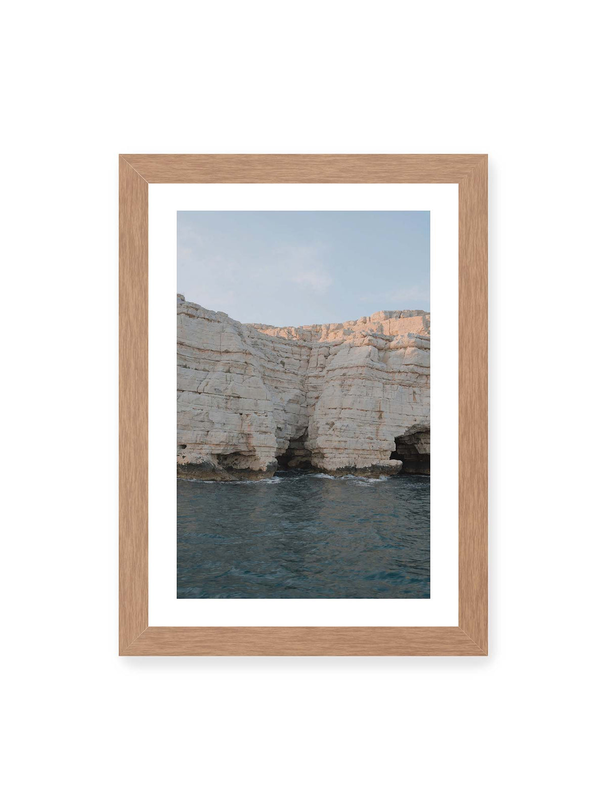 21x30 cm, weißer Galerie-Rand, Eichenrahmen – Helle geschichtete Felswand mit dunklen Grotten über bewegtem blauem Meer und blassem Himmel.