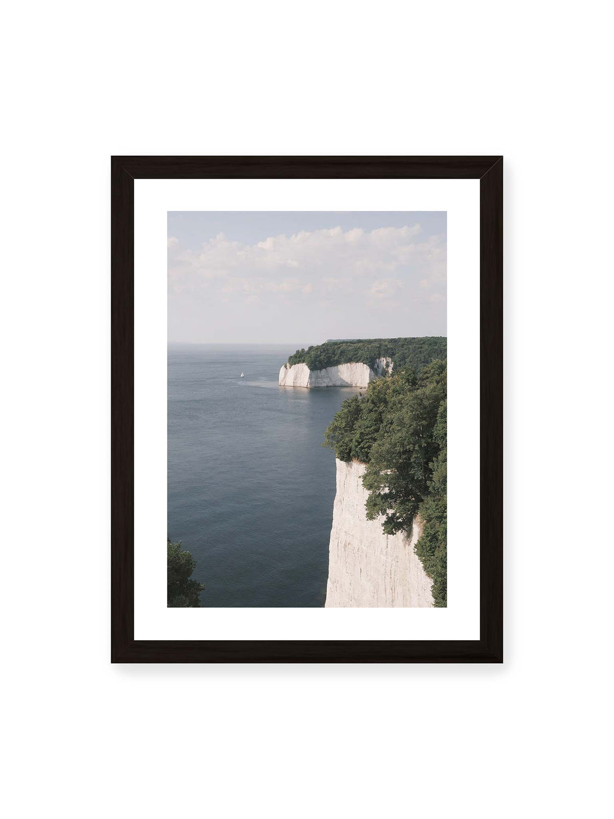 30x40 cm, weißer Galerie-Rand, schwarzer Rahmen – Helle Steilklippen mit grünen Baumkronen über ruhigem blauem Meer und einem kleinen Segelboot.