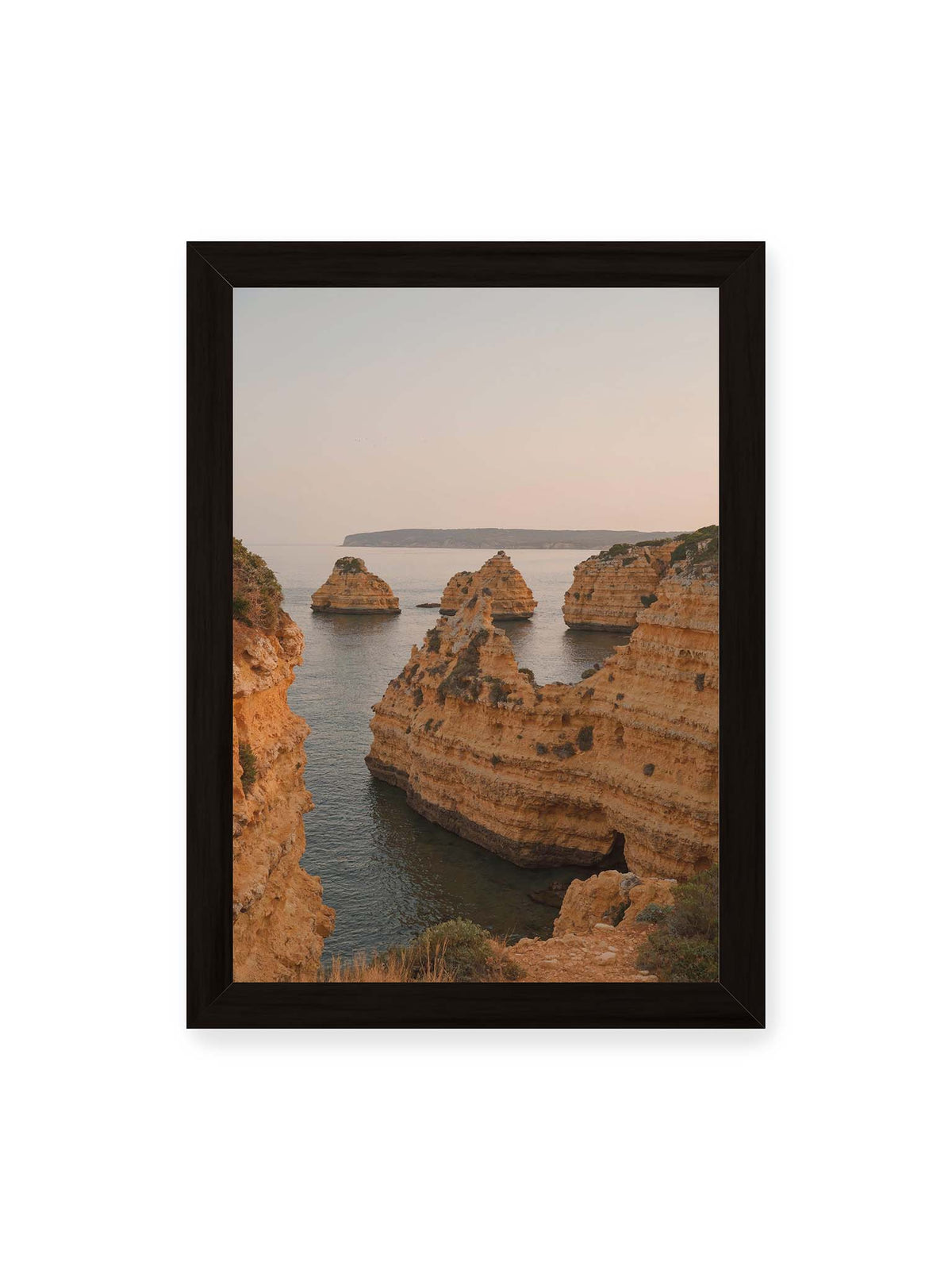21x30 cm, schwarzer Rahmen – Warm getönte, geschichtete Felsformationen ragen zwischen steilen Küstenwänden aus ruhigem Meer.