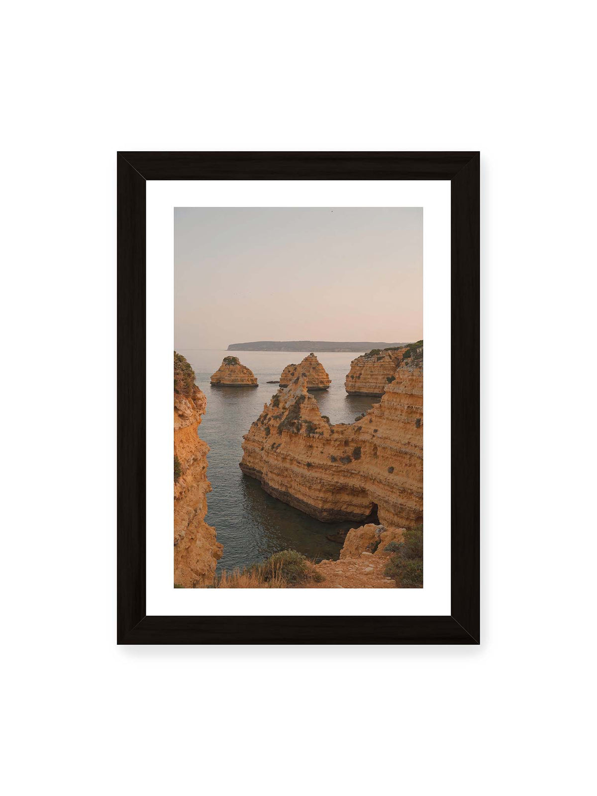 21x30 cm, weißer Galerie-Rand, schwarzer Rahmen – Warm getönte, geschichtete Felsformationen ragen zwischen steilen Küstenwänden aus ruhigem Meer.