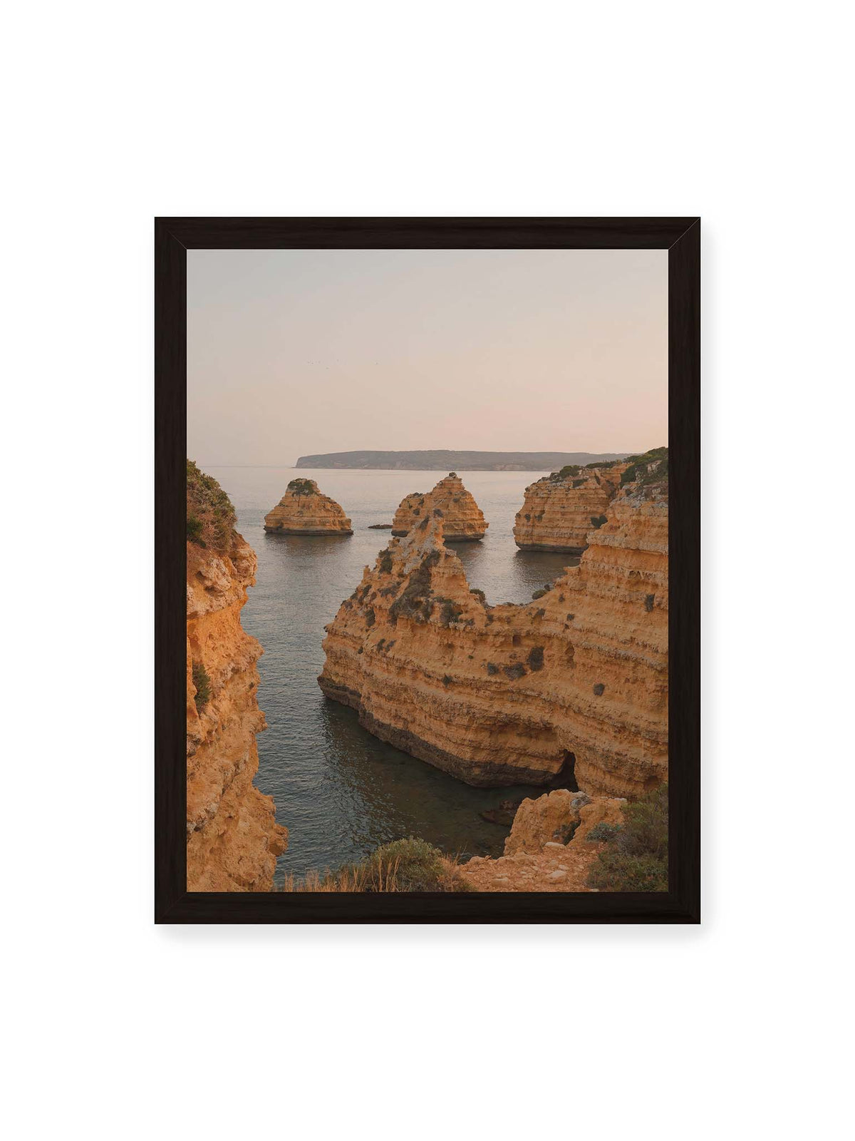 30x40 cm, schwarzer Rahmen – Warm getönte, geschichtete Felsformationen ragen zwischen steilen Küstenwänden aus ruhigem Meer.