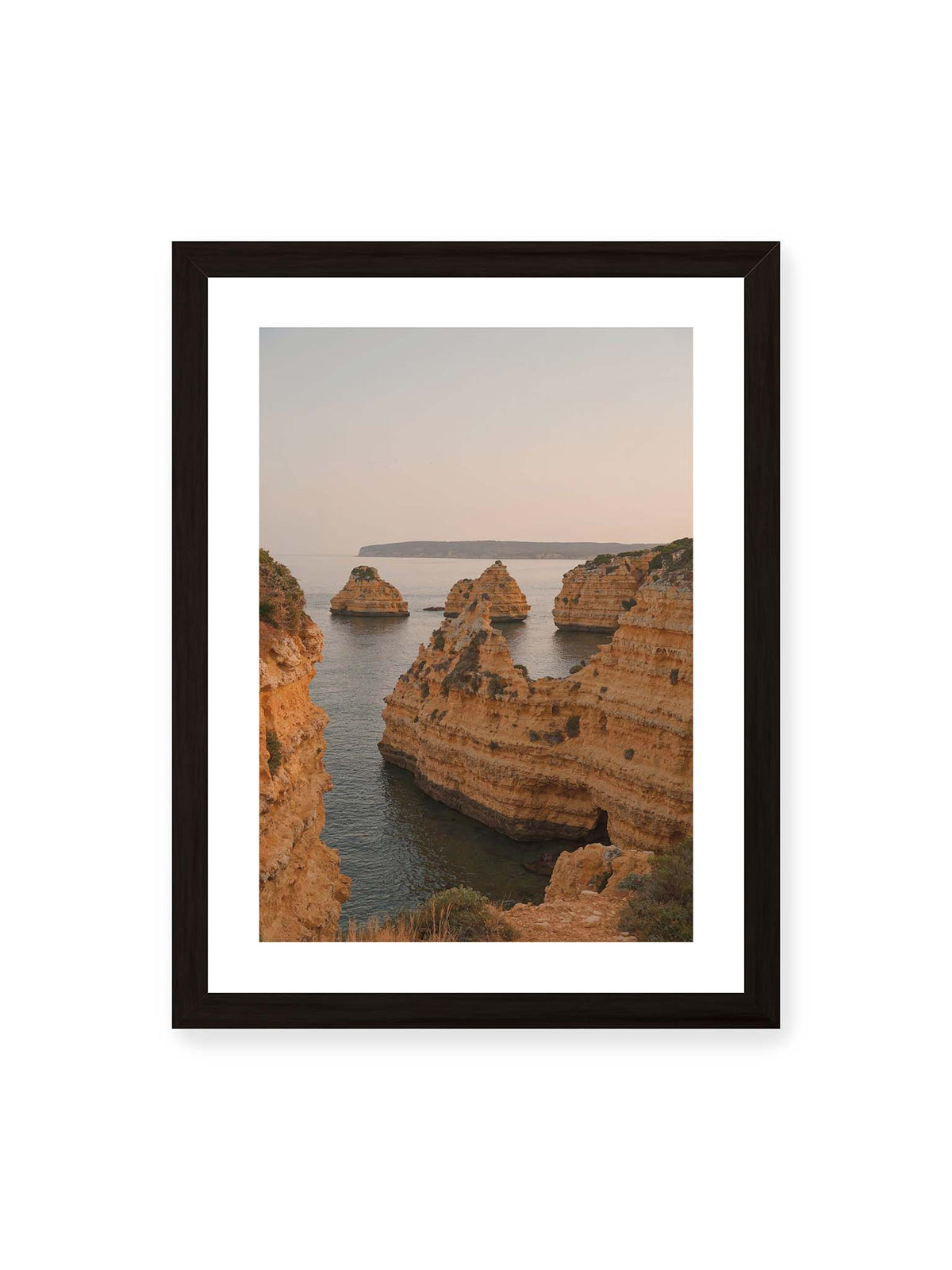 30x40 cm, weißer Galerie-Rand, schwarzer Rahmen – Warm getönte, geschichtete Felsformationen ragen zwischen steilen Küstenwänden aus ruhigem Meer.