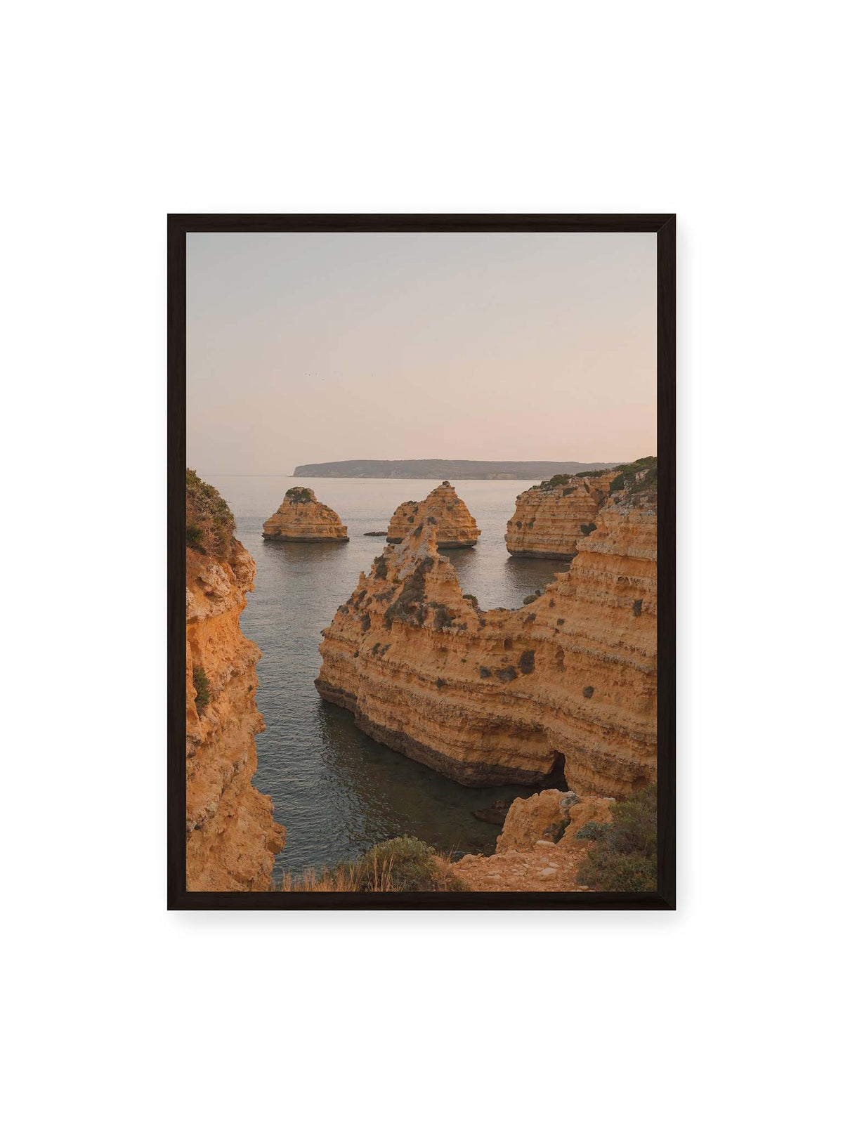 50x70 cm, schwarzer Rahmen – Warm getönte, geschichtete Felsformationen ragen zwischen steilen Küstenwänden aus ruhigem Meer.