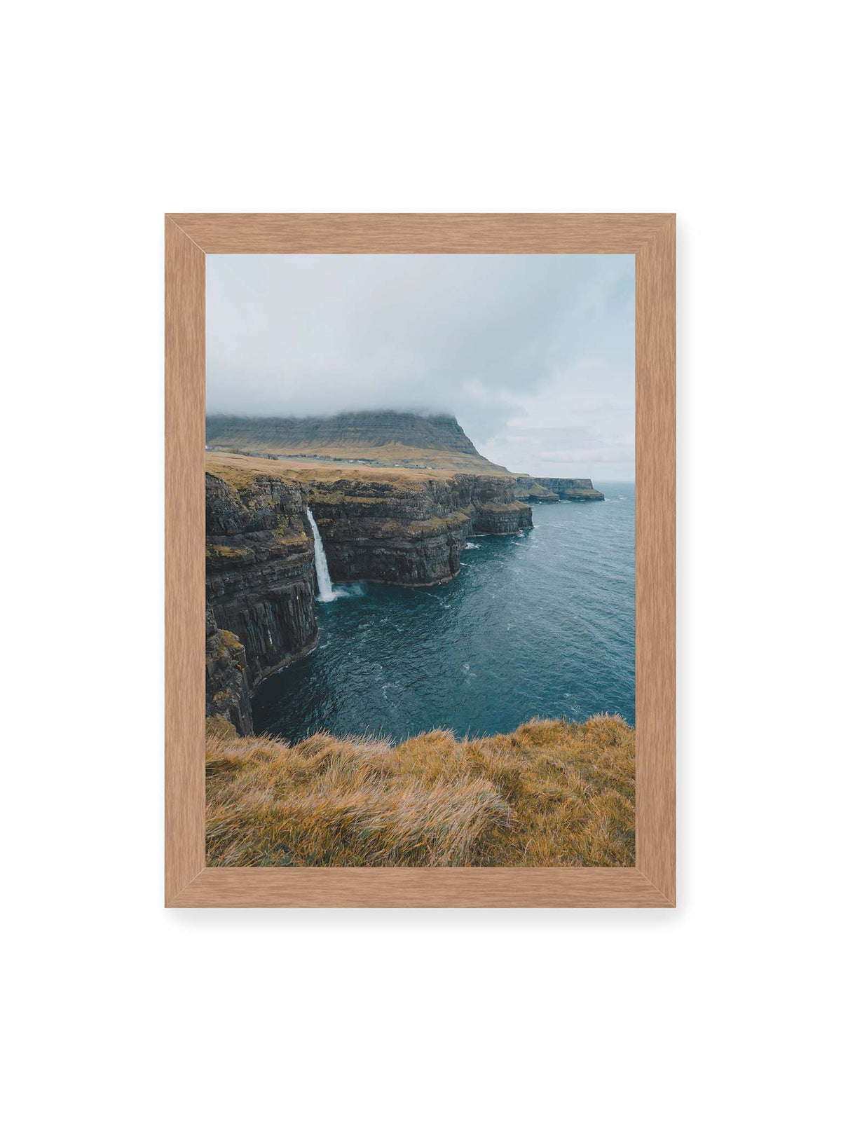 21x30 cm, Eichenrahmen – Dunkle Küstenklippen mit Wasserfall, grasigem Hochland und tief hängenden Wolken über blauem Meer.