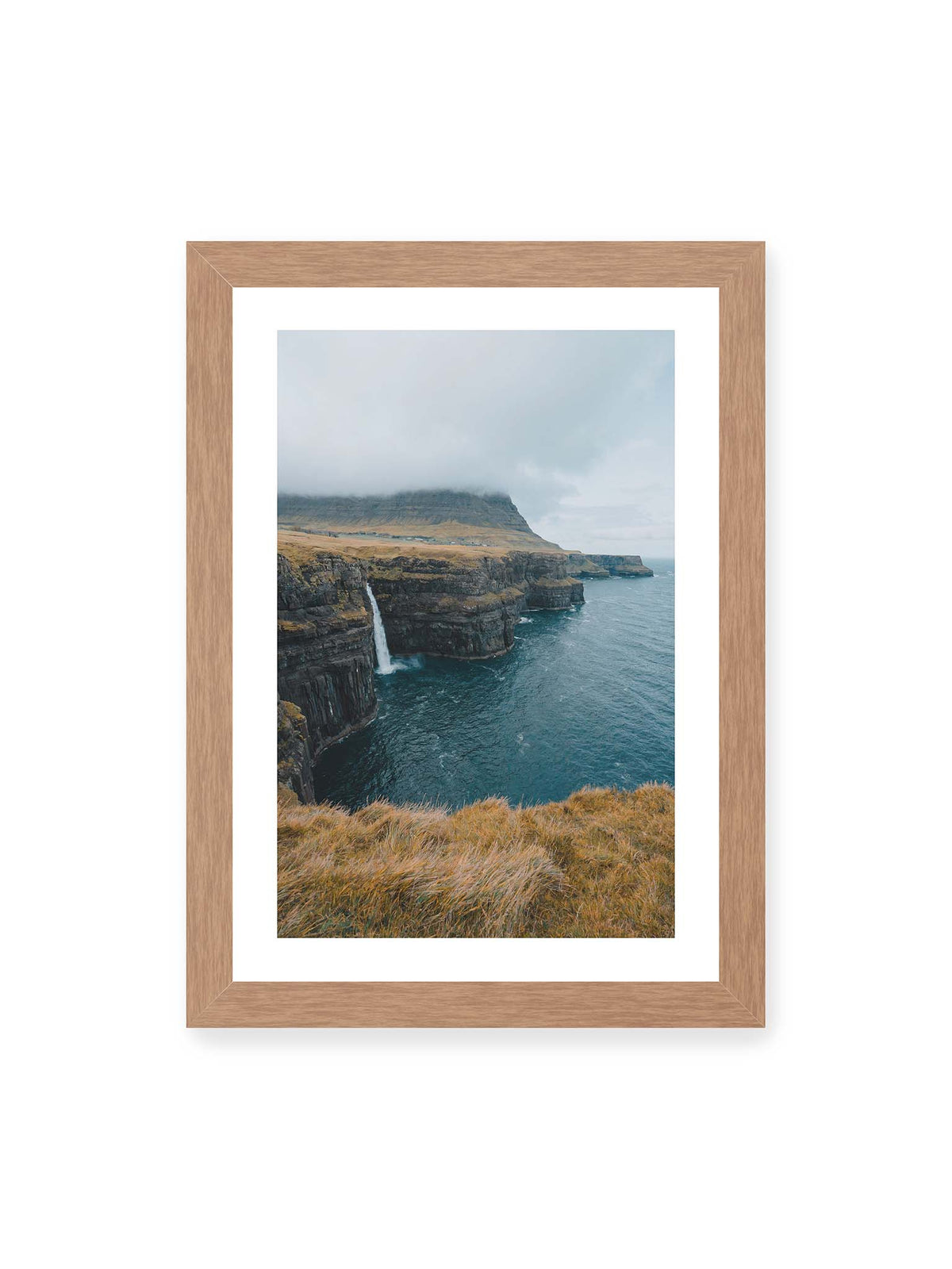 21x30 cm, weißer Galerie-Rand, Eichenrahmen – Dunkle Küstenklippen mit Wasserfall, grasigem Hochland und tief hängenden Wolken über blauem Meer.