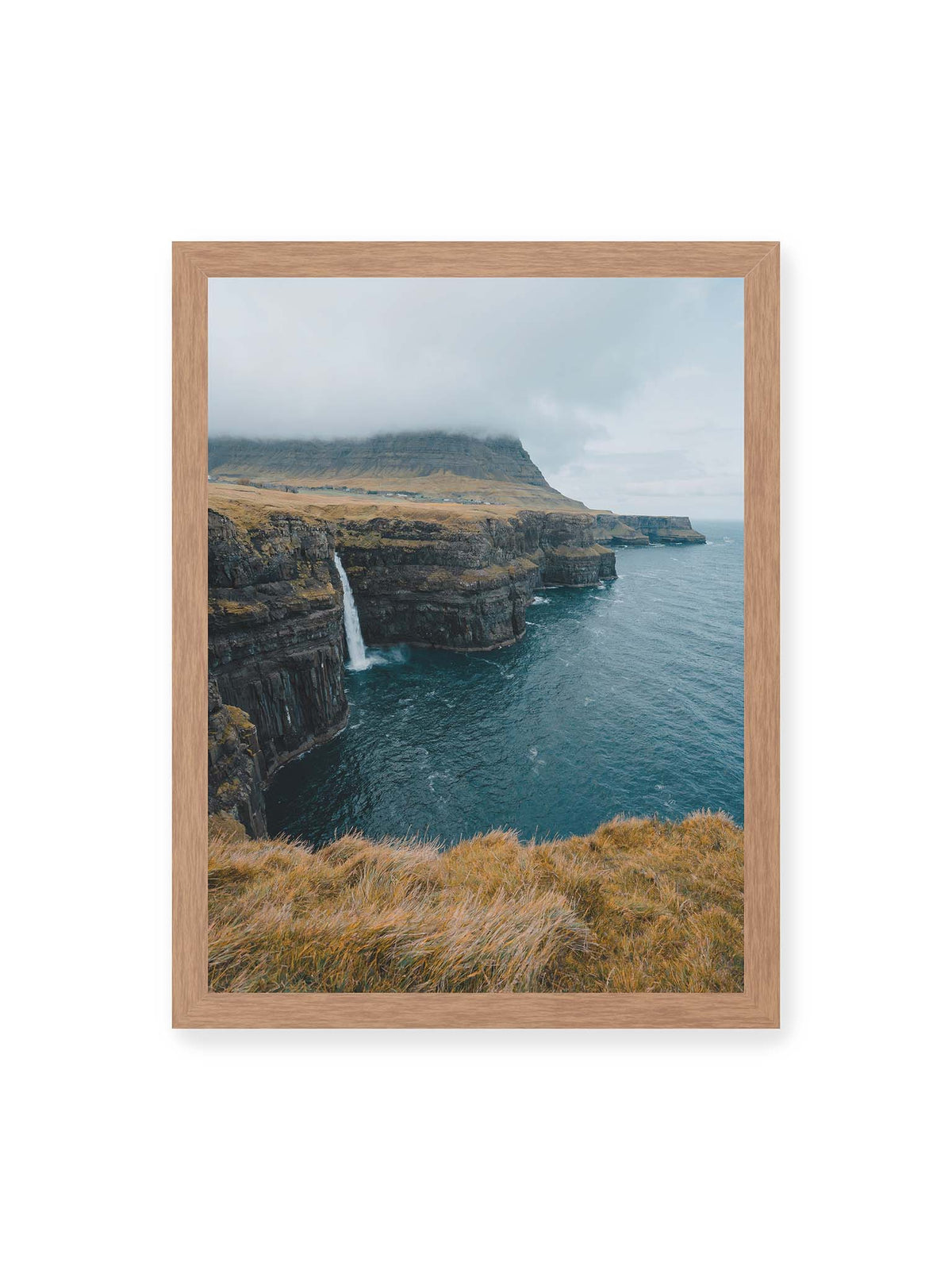 30x40 cm, Eichenrahmen – Dunkle Küstenklippen mit Wasserfall, grasigem Hochland und tief hängenden Wolken über blauem Meer.