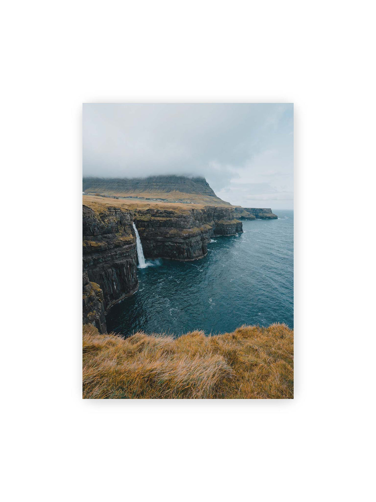 50x70 cm – Dunkle Küstenklippen mit Wasserfall, grasigem Hochland und tief hängenden Wolken über blauem Meer.
