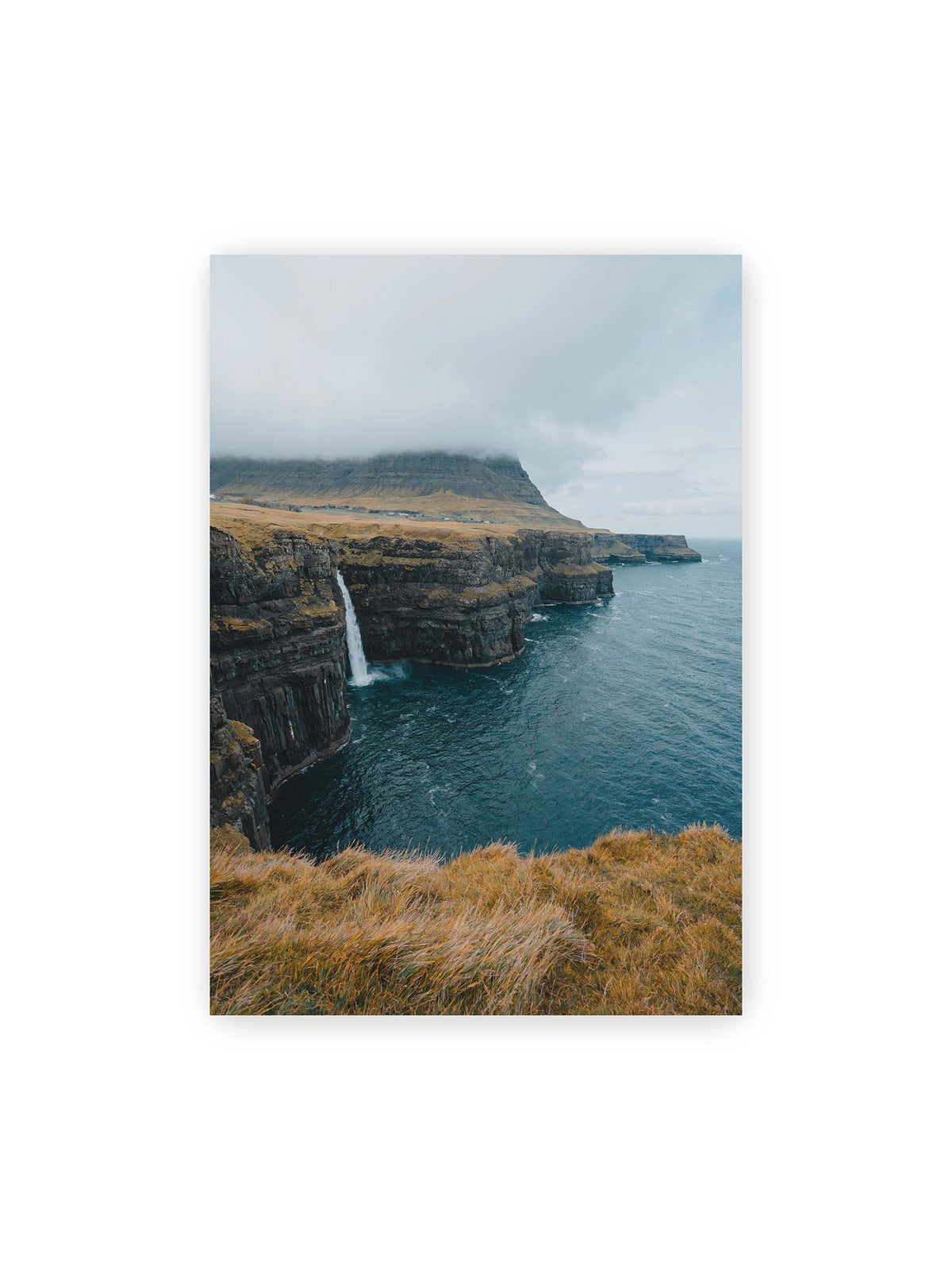 70x100 cm – Dunkle Küstenklippen mit Wasserfall, grasigem Hochland und tief hängenden Wolken über blauem Meer.