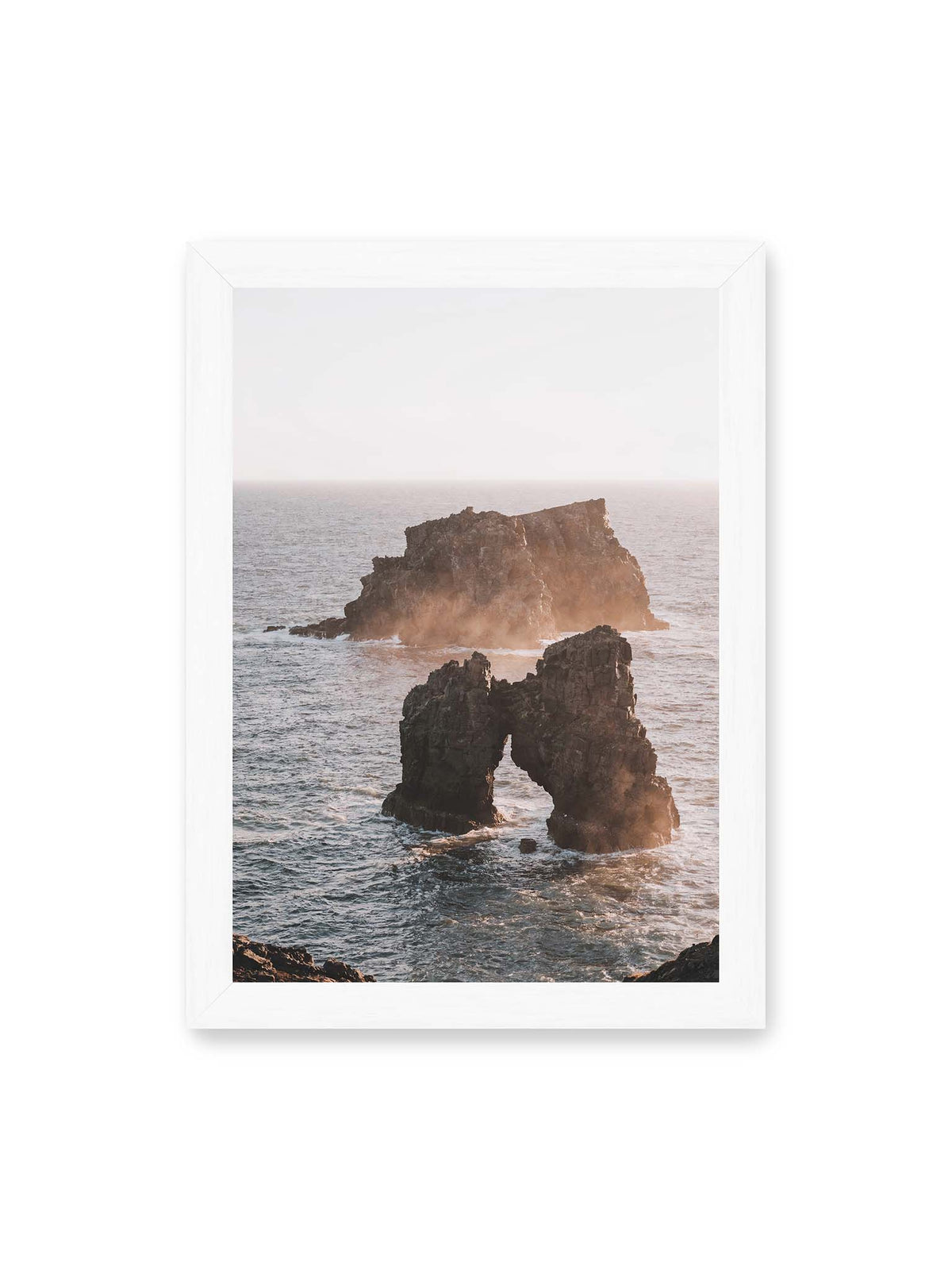 21x30 cm, weißer Rahmen – Dunkler Felsbogen und massive Felsformation im bewegten Meer, umgeben von heller Gischt und warmem Licht.