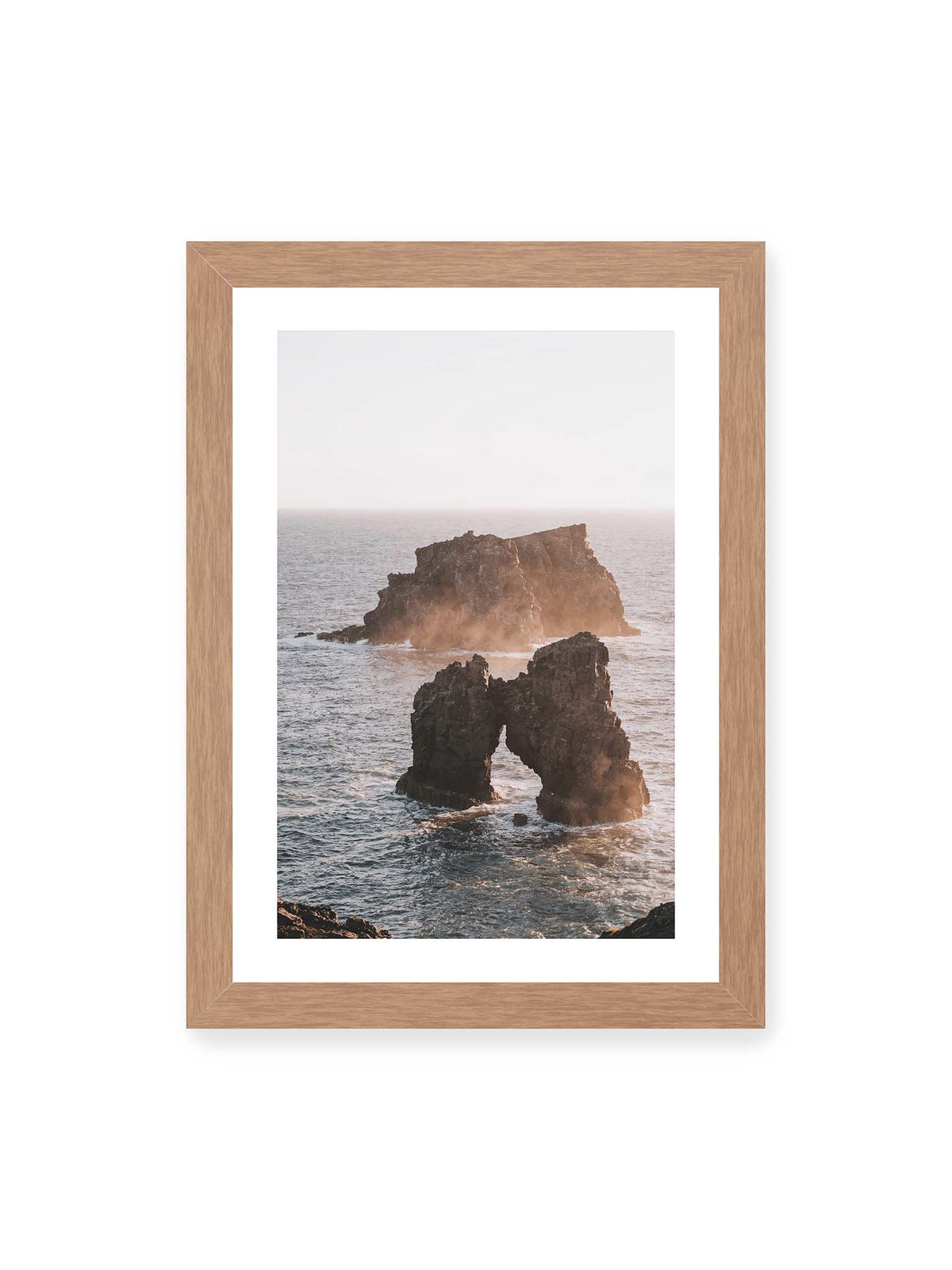 21x30 cm, weißer Galerie-Rand, Eichenrahmen – Dunkler Felsbogen und massive Felsformation im bewegten Meer, umgeben von heller Gischt und warmem Licht.
