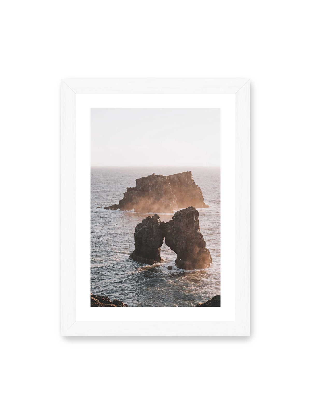 21x30 cm, weißer Galerie-Rand, weißer Rahmen – Dunkler Felsbogen und massive Felsformation im bewegten Meer, umgeben von heller Gischt und warmem Licht.