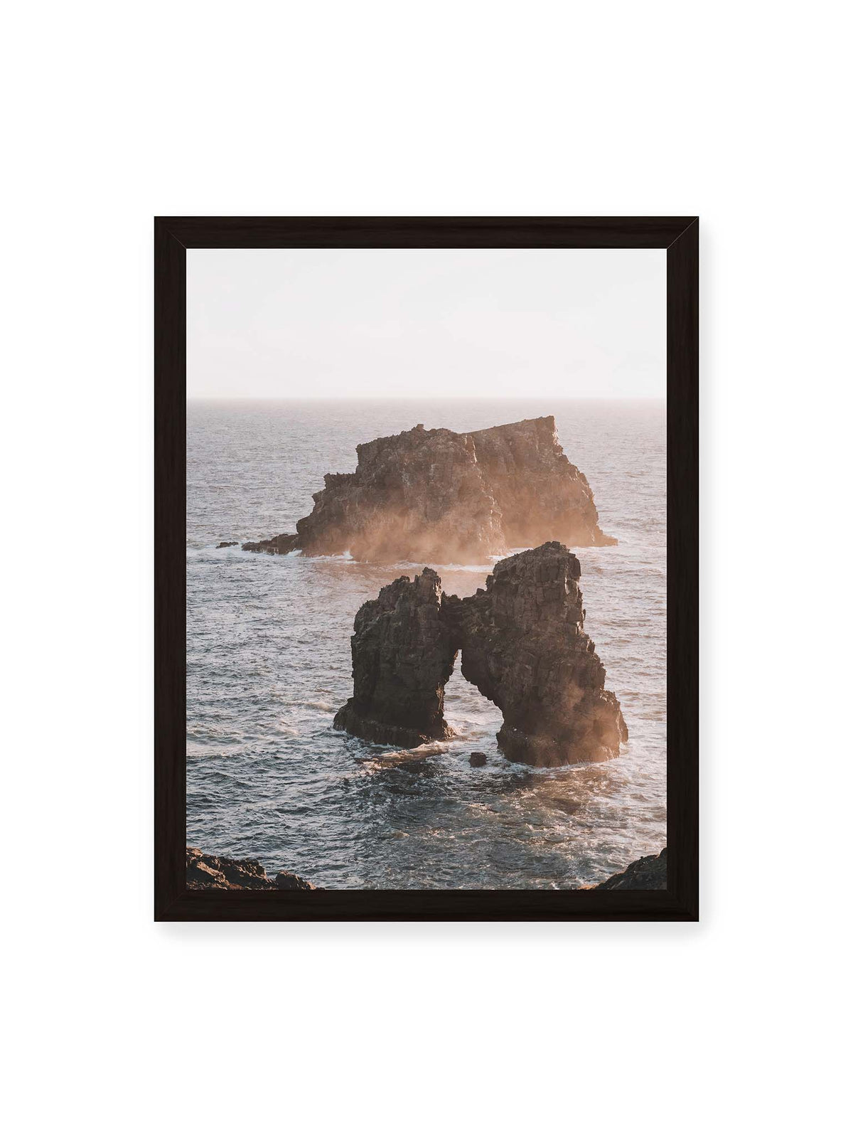 30x40 cm, schwarzer Rahmen – Dunkler Felsbogen und massive Felsformation im bewegten Meer, umgeben von heller Gischt und warmem Licht.