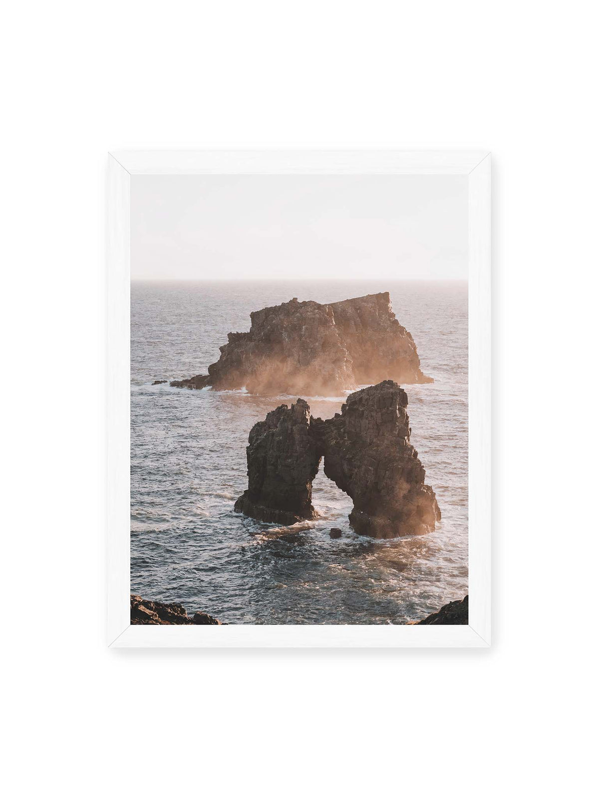 30x40 cm, weißer Rahmen – Dunkler Felsbogen und massive Felsformation im bewegten Meer, umgeben von heller Gischt und warmem Licht.