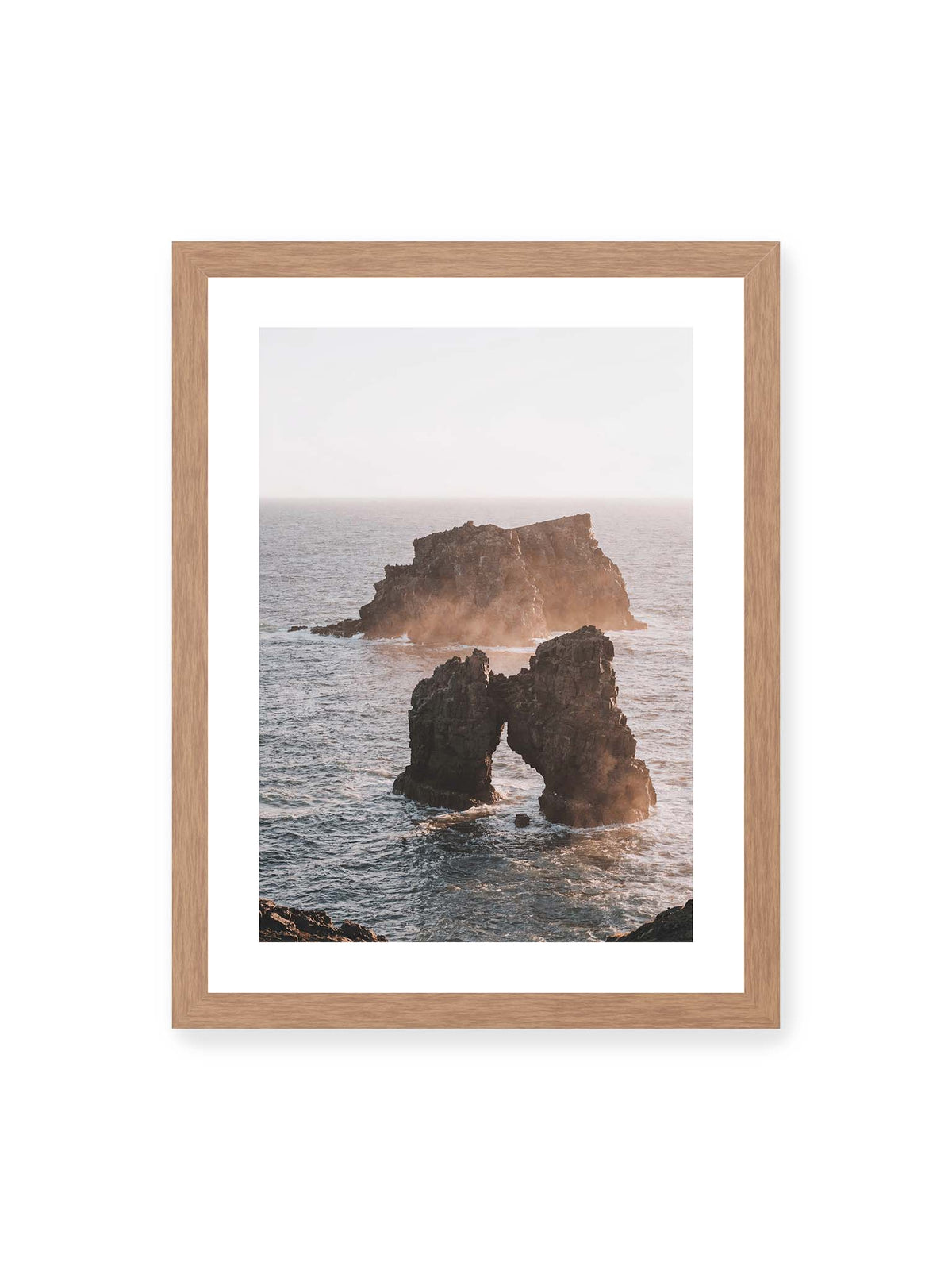 30x40 cm, weißer Galerie-Rand, Eichenrahmen – Dunkler Felsbogen und massive Felsformation im bewegten Meer, umgeben von heller Gischt und warmem Licht.