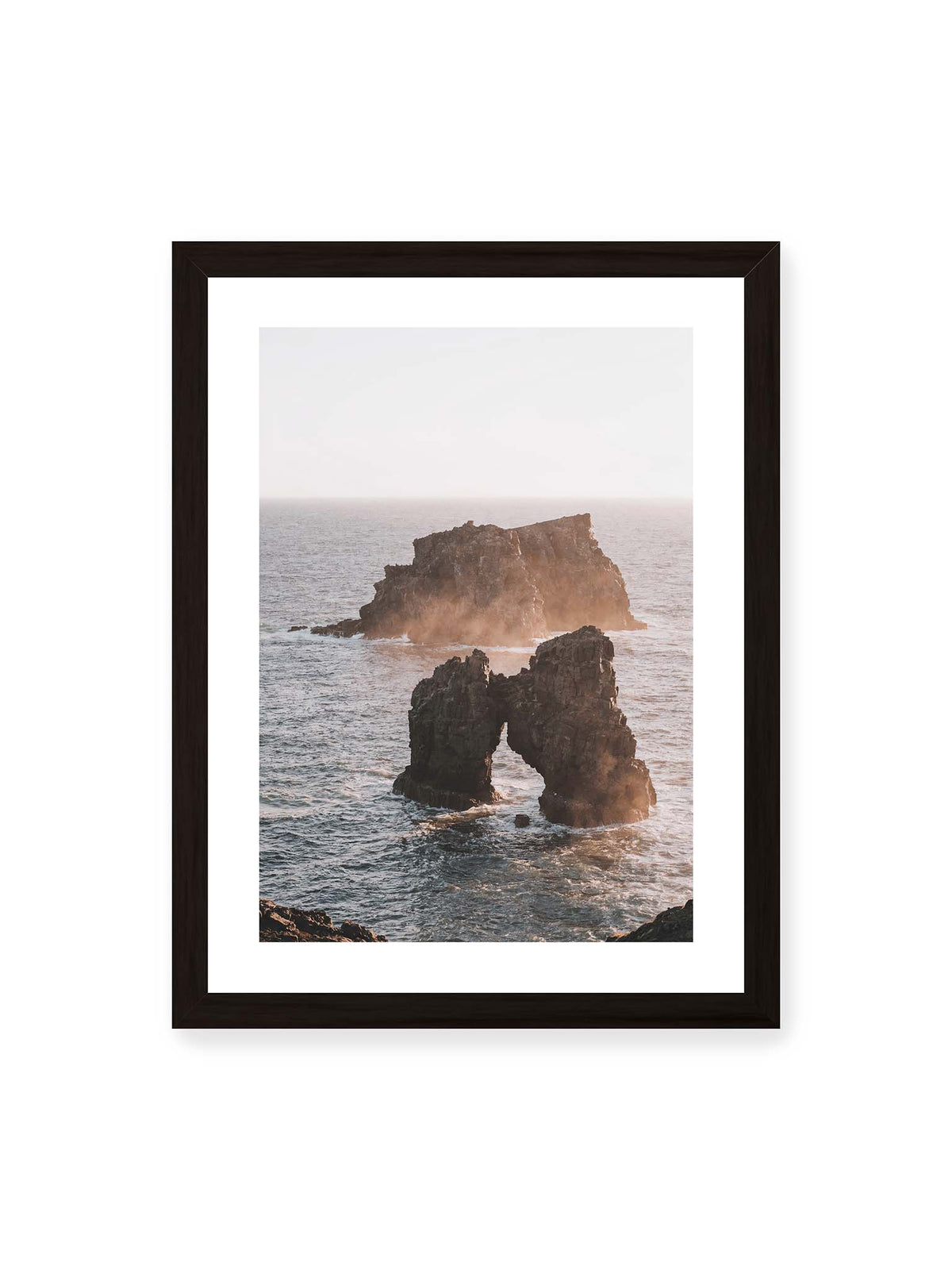 30x40 cm, weißer Galerie-Rand, schwarzer Rahmen – Dunkler Felsbogen und massive Felsformation im bewegten Meer, umgeben von heller Gischt und warmem Licht.
