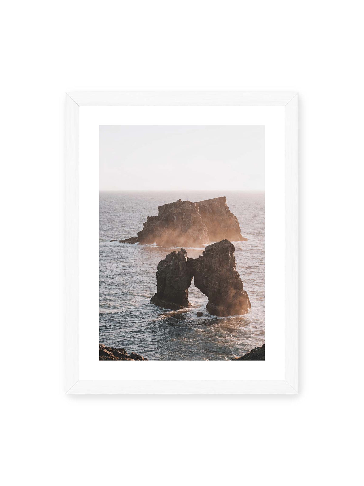 30x40 cm, weißer Galerie-Rand, weißer Rahmen – Dunkler Felsbogen und massive Felsformation im bewegten Meer, umgeben von heller Gischt und warmem Licht.