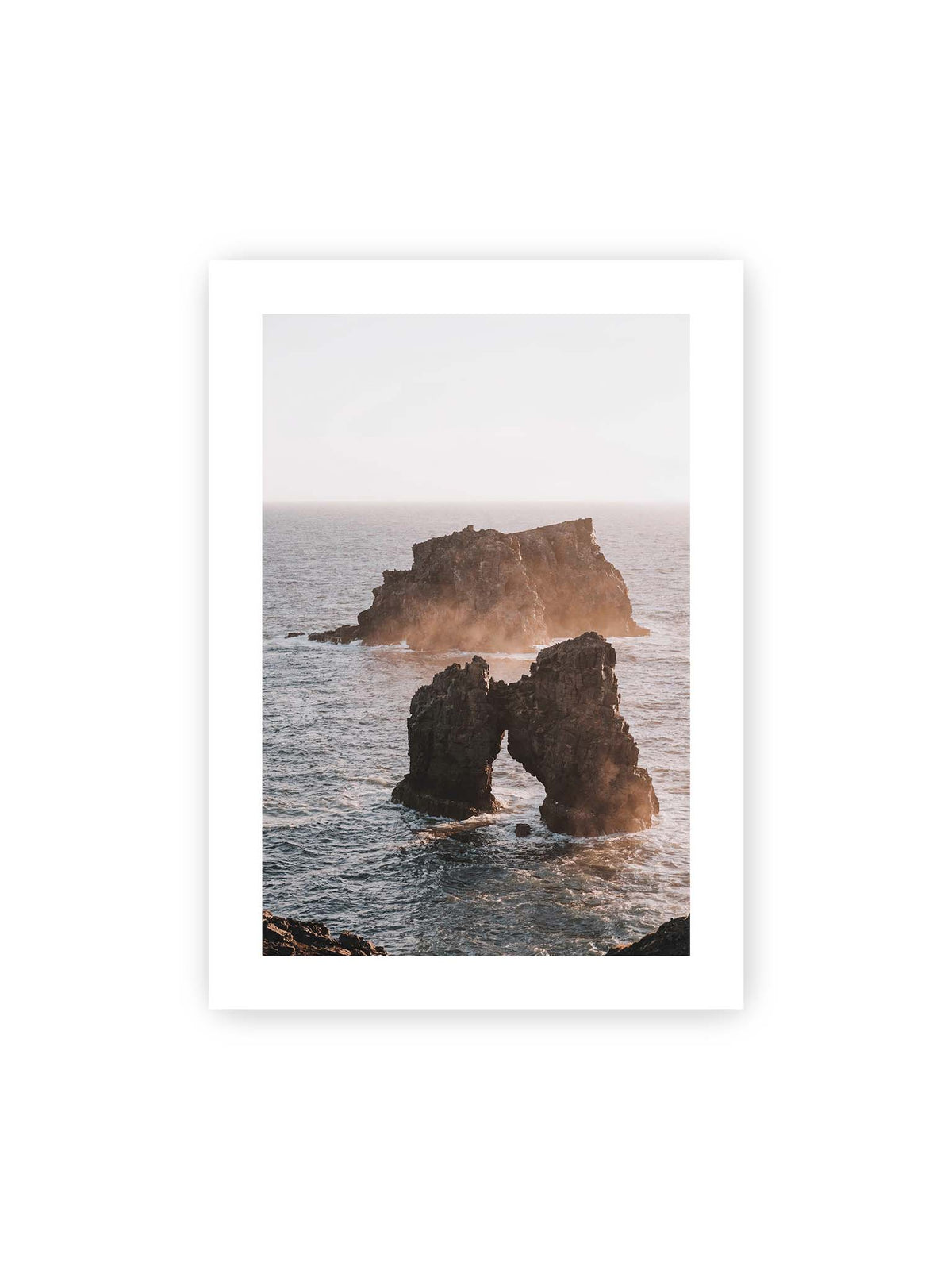 50x70 cm, weißer Galerie-Rand – Dunkler Felsbogen und massive Felsformation im bewegten Meer, umgeben von heller Gischt und warmem Licht.