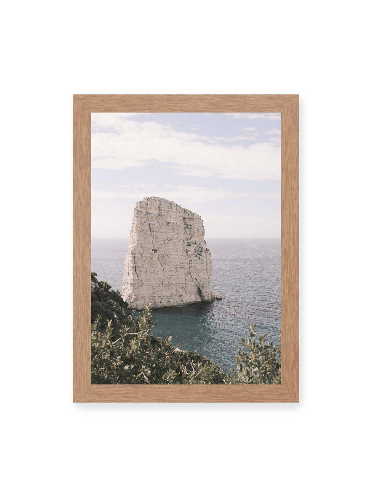 21x30 cm, Eichenrahmen – Heller, steil aufragender Felsen im Meer vor blassem Himmel, eingerahmt von grüner Vegetation.