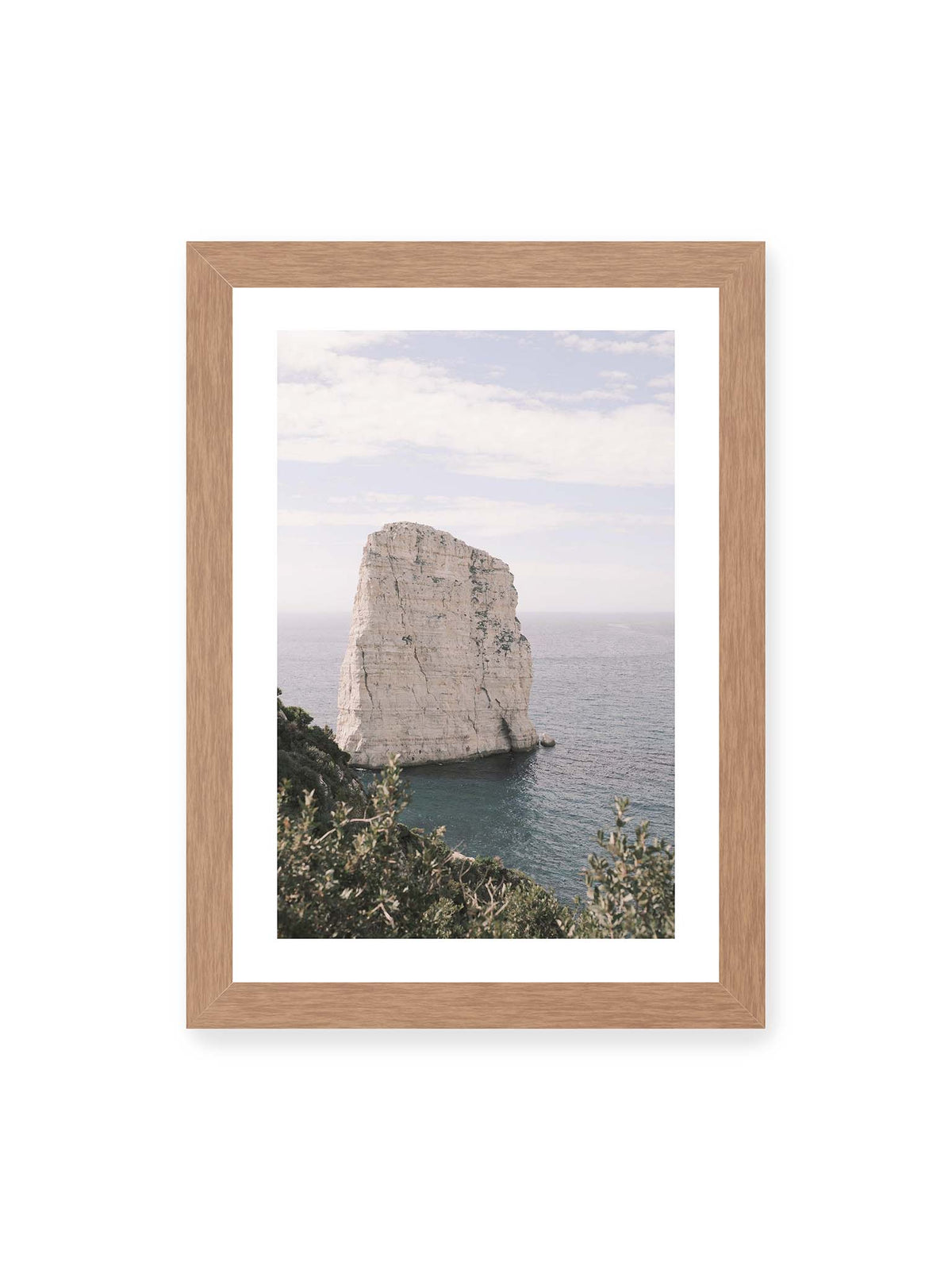 21x30 cm, weißer Galerie-Rand, Eichenrahmen – Heller, steil aufragender Felsen im Meer vor blassem Himmel, eingerahmt von grüner Vegetation.