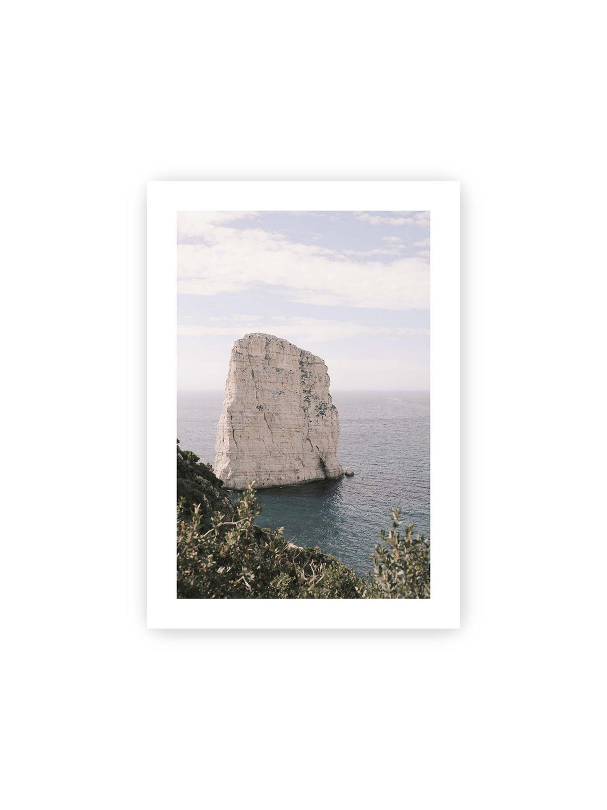 21x30 cm, weißer Galerie-Rand – Heller, steil aufragender Felsen im Meer vor blassem Himmel, eingerahmt von grüner Vegetation.
