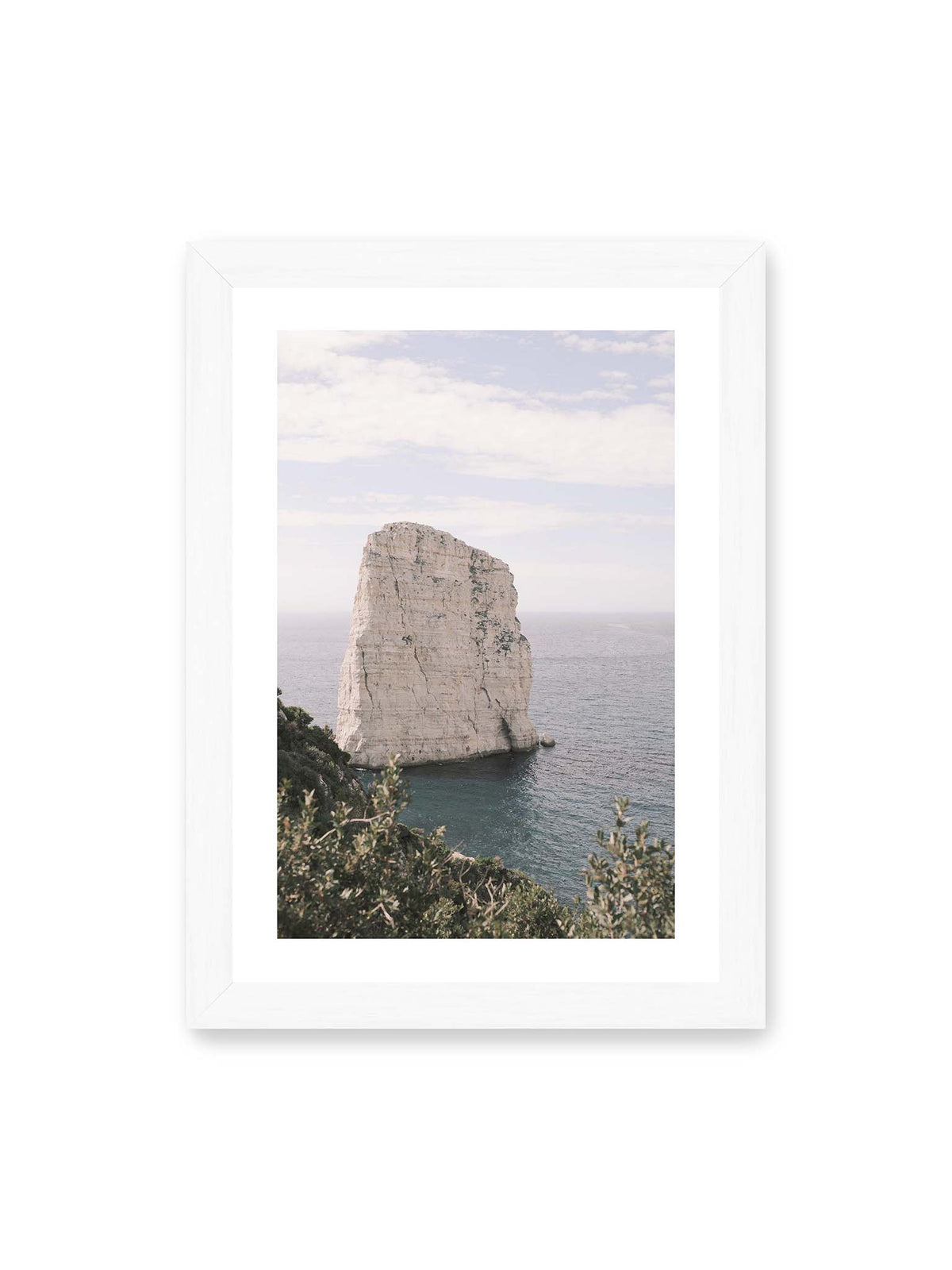 21x30 cm, weißer Galerie-Rand, weißer Rahmen – Heller, steil aufragender Felsen im Meer vor blassem Himmel, eingerahmt von grüner Vegetation.
