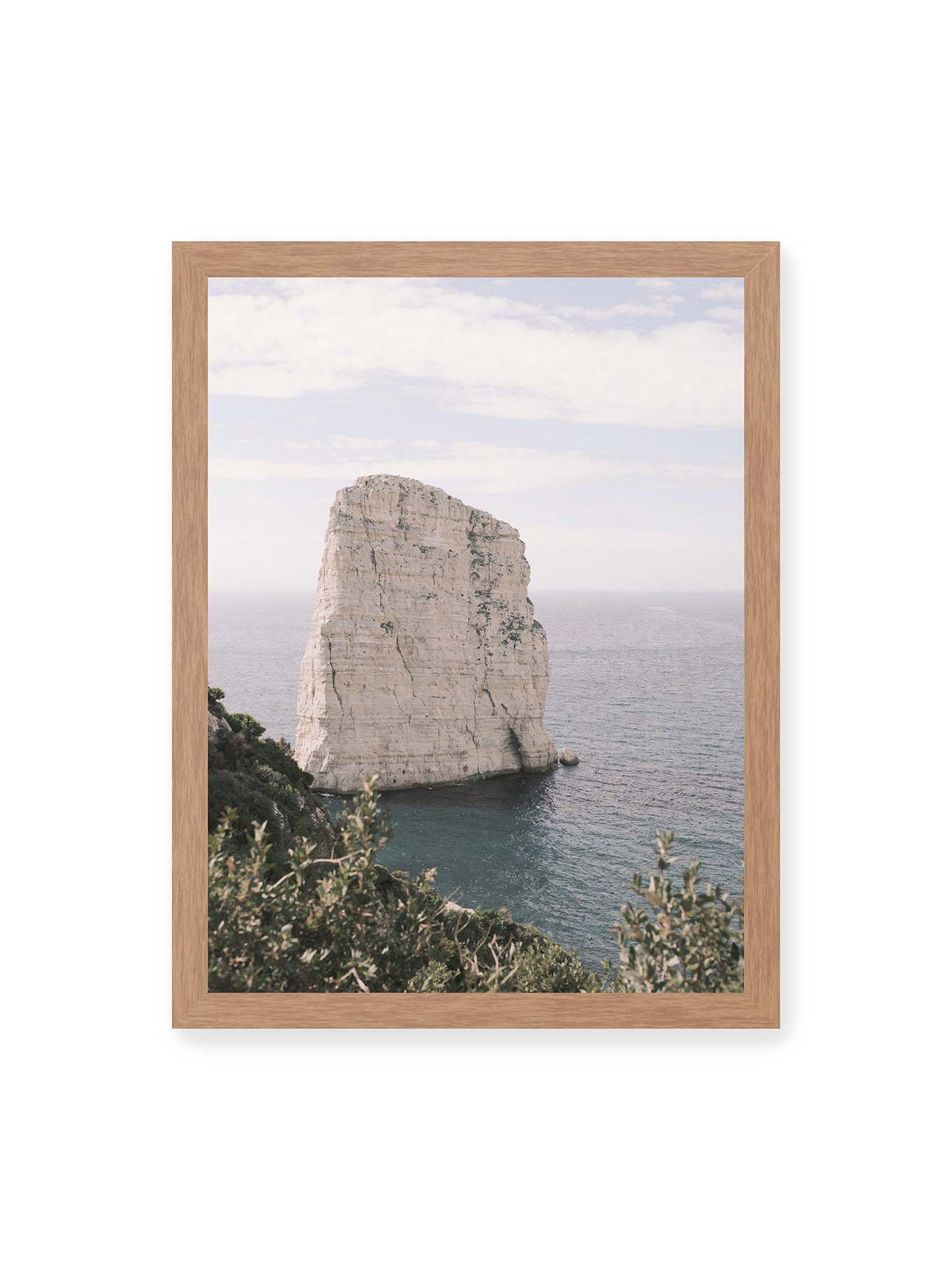 30x40 cm, Eichenrahmen – Heller, steil aufragender Felsen im Meer vor blassem Himmel, eingerahmt von grüner Vegetation.