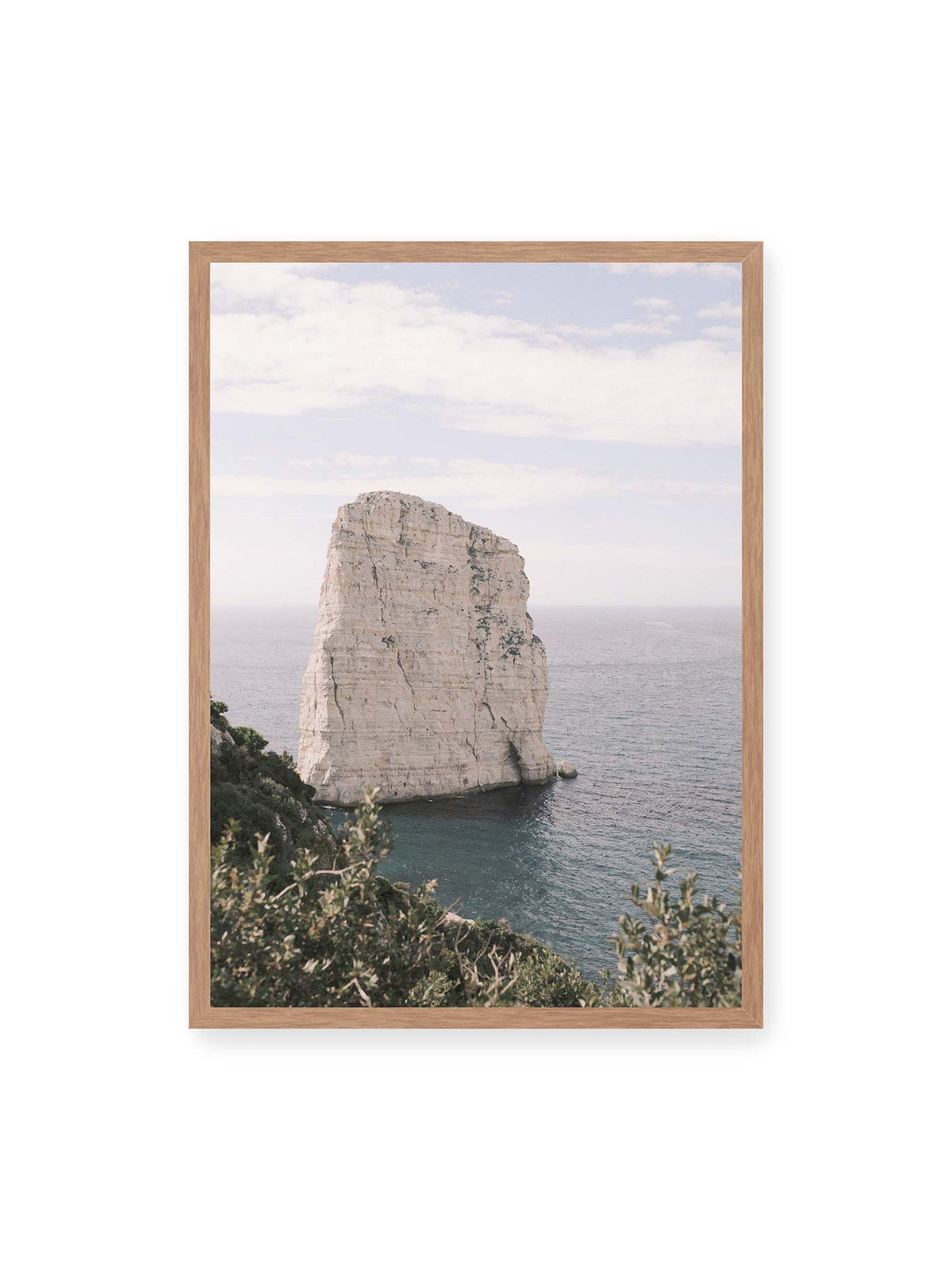 50x70 cm, Eichenrahmen – Heller, steil aufragender Felsen im Meer vor blassem Himmel, eingerahmt von grüner Vegetation.