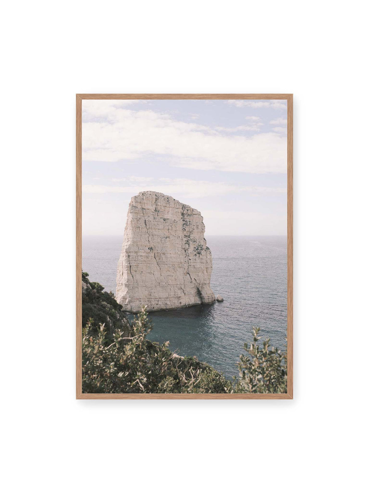 70x100 cm, Eichenrahmen – Heller, steil aufragender Felsen im Meer vor blassem Himmel, eingerahmt von grüner Vegetation.
