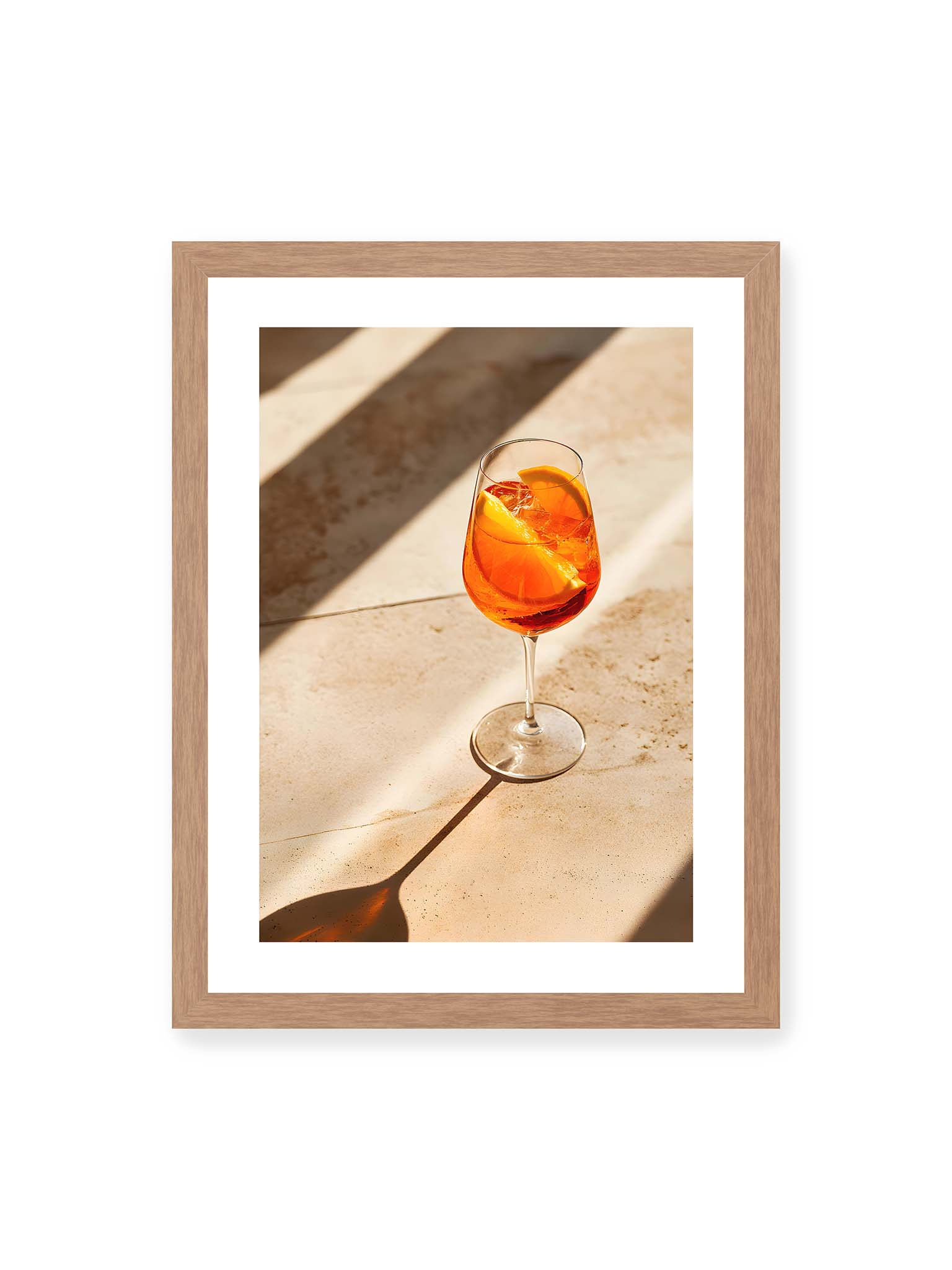30x40 cm, weißer Galerie-Rand, Eichenrahmen – Aperitifglas mit orangefarbenem Drink und Orangenscheiben, Sonnenlicht und langer Schatten auf hellem Stein.