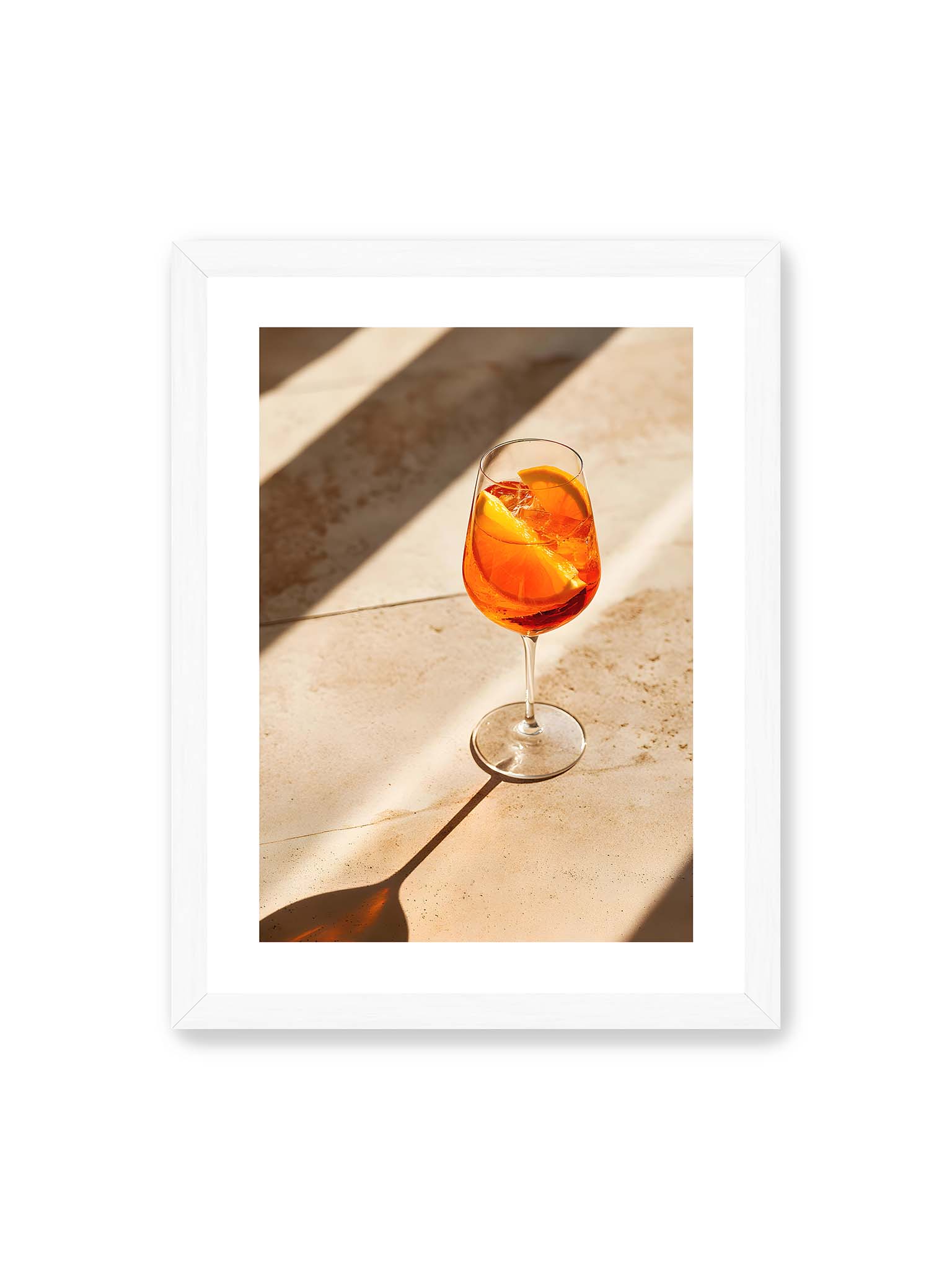 30x40 cm, weißer Galerie-Rand, weißer Rahmen – Aperitifglas mit orangefarbenem Drink und Orangenscheiben, Sonnenlicht und langer Schatten auf hellem Stein.