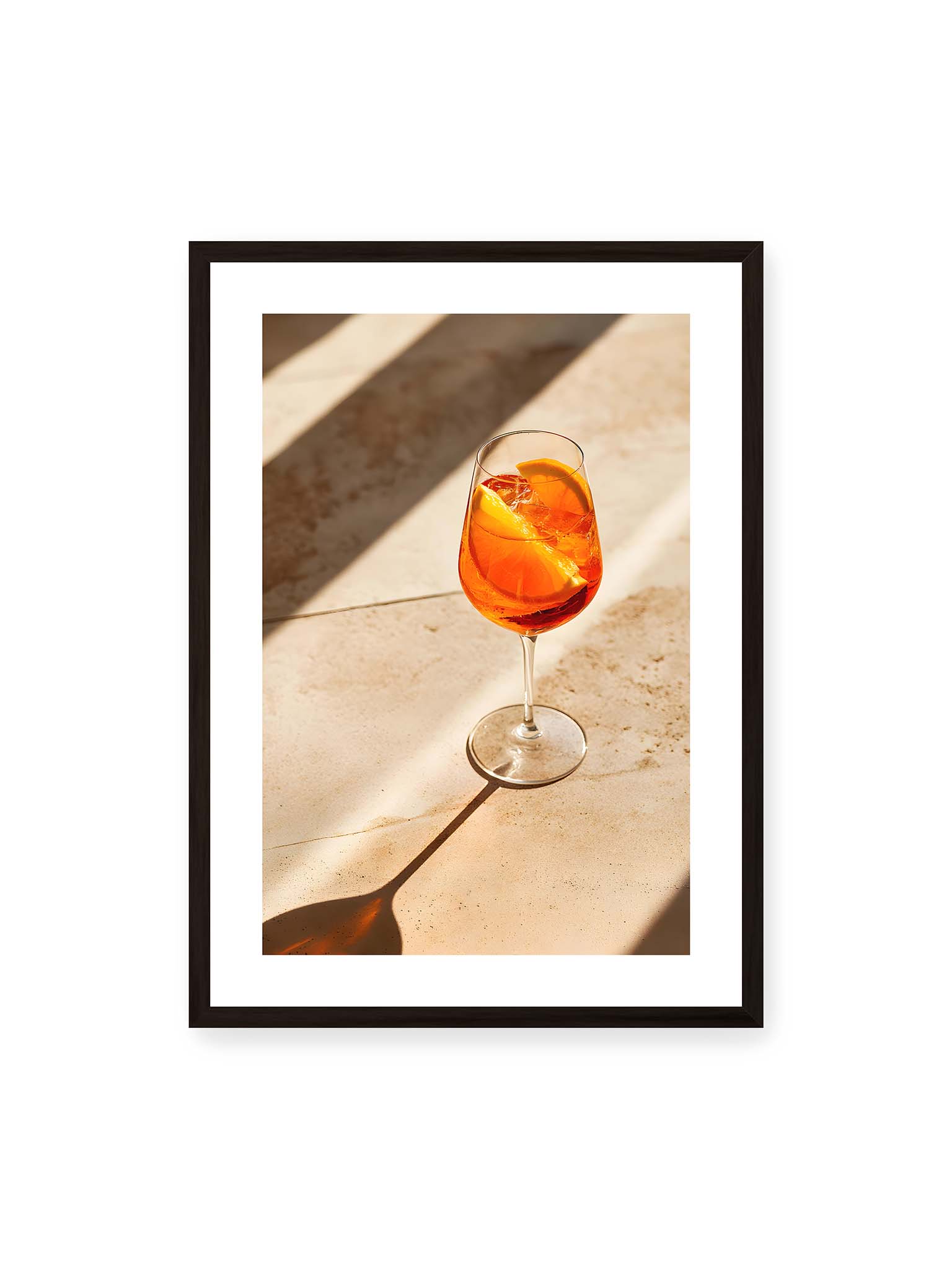50x70 cm, weißer Galerie-Rand, schwarzer Rahmen – Aperitifglas mit orangefarbenem Drink und Orangenscheiben, Sonnenlicht und langer Schatten auf hellem Stein.