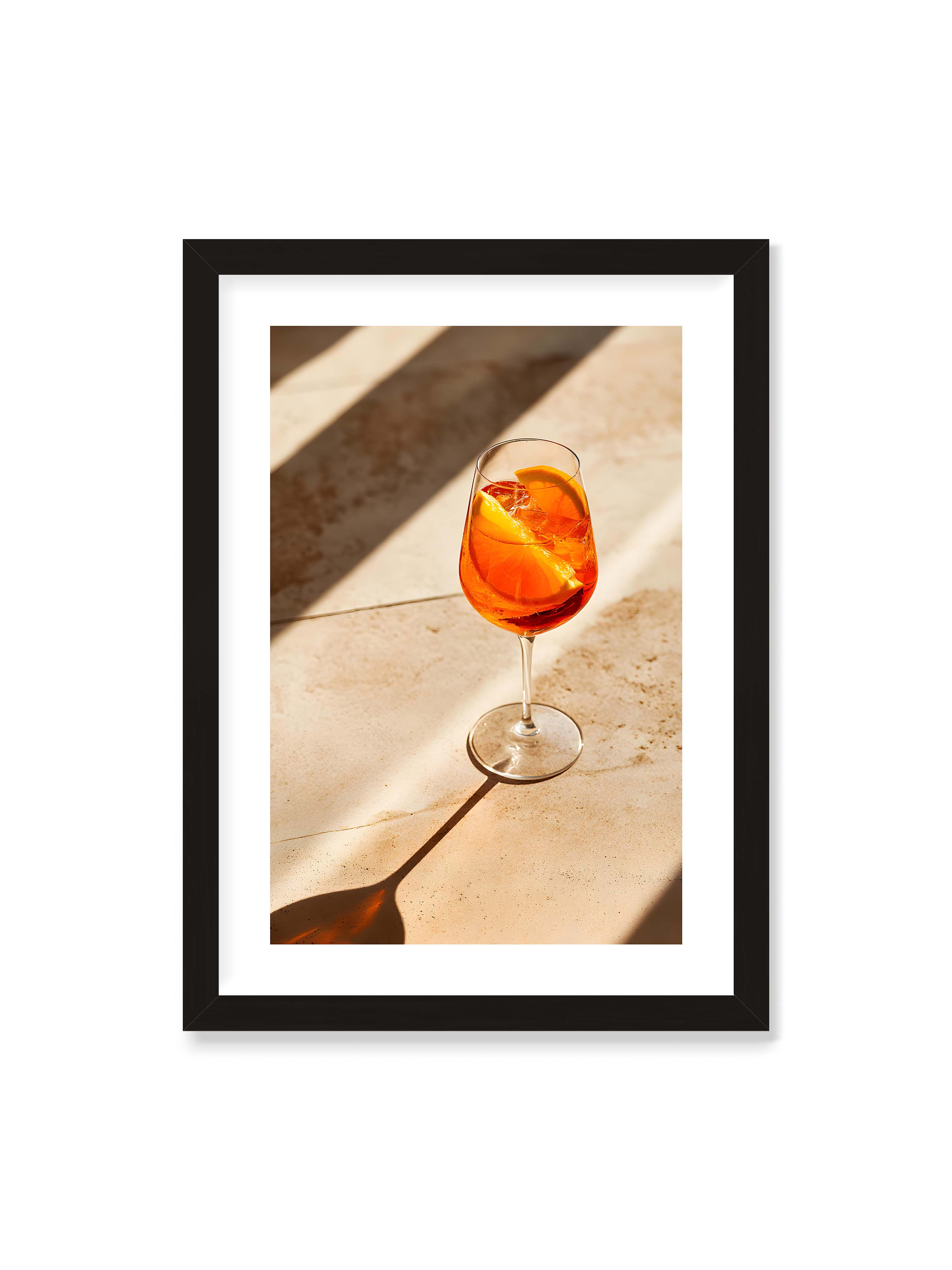 50x70 cm mit weißem Galerie-Rand mit schwarzem Rahmen – Aperitifglas mit orangefarbenem Drink und Orangenscheiben, Sonnenlicht und langer Schatten auf hellem Stein.