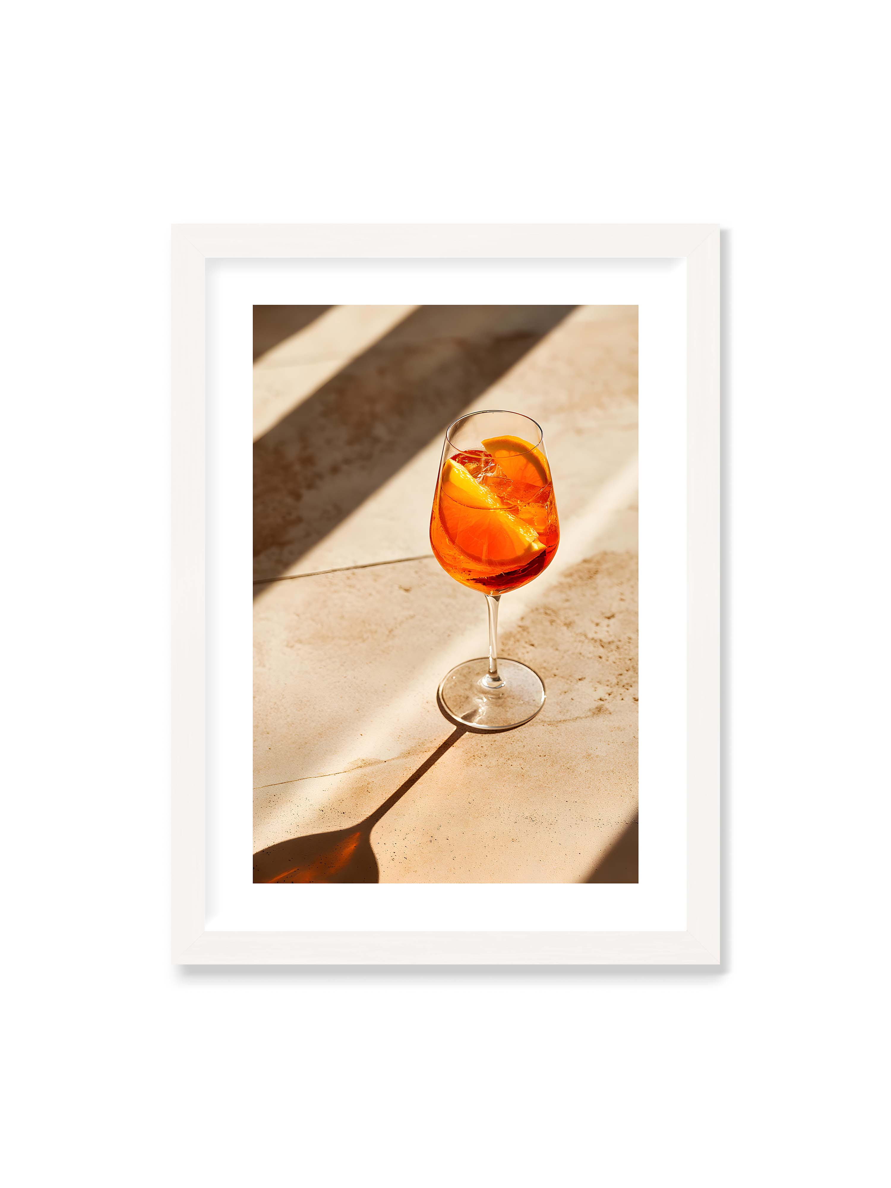 50x70 cm mit weißem Galerie-Rand mit weißem Rahmen – Aperitifglas mit orangefarbenem Drink und Orangenscheiben, Sonnenlicht und langer Schatten auf hellem Stein.