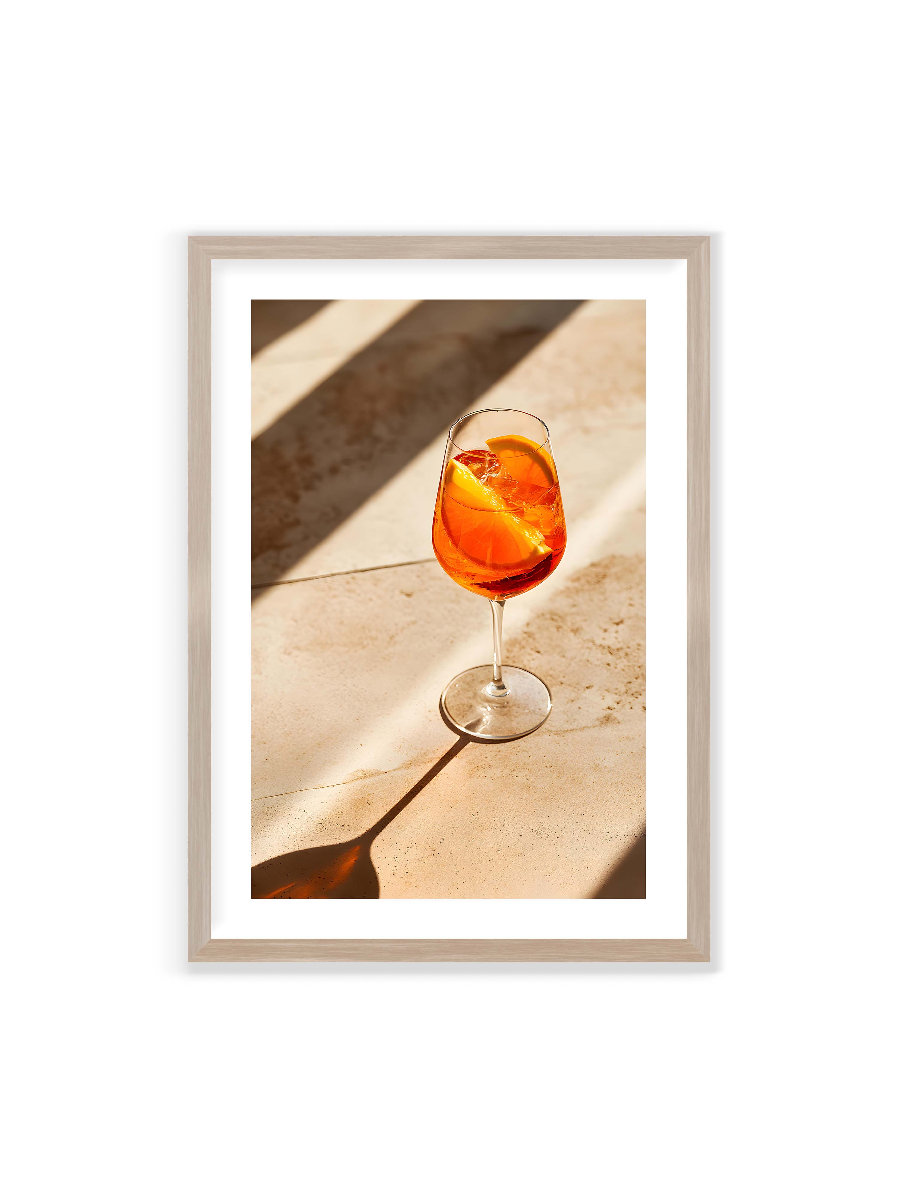 70x100 cm mit weißem Galerie-Rand im Eichenrahmen – Aperitifglas mit orangefarbenem Drink und Orangenscheiben, Sonnenlicht und langer Schatten auf hellem Stein.