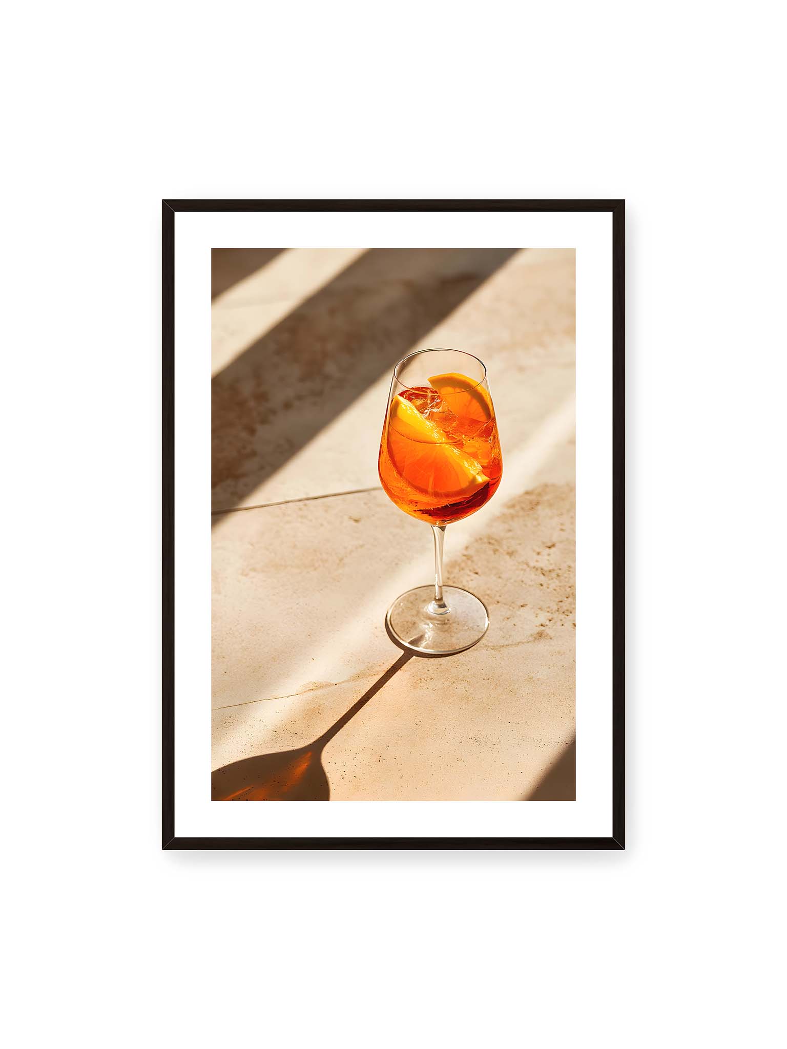 70x100 cm, weißer Galerie-Rand, schwarzer Rahmen – Aperitifglas mit orangefarbenem Drink und Orangenscheiben, Sonnenlicht und langer Schatten auf hellem Stein.