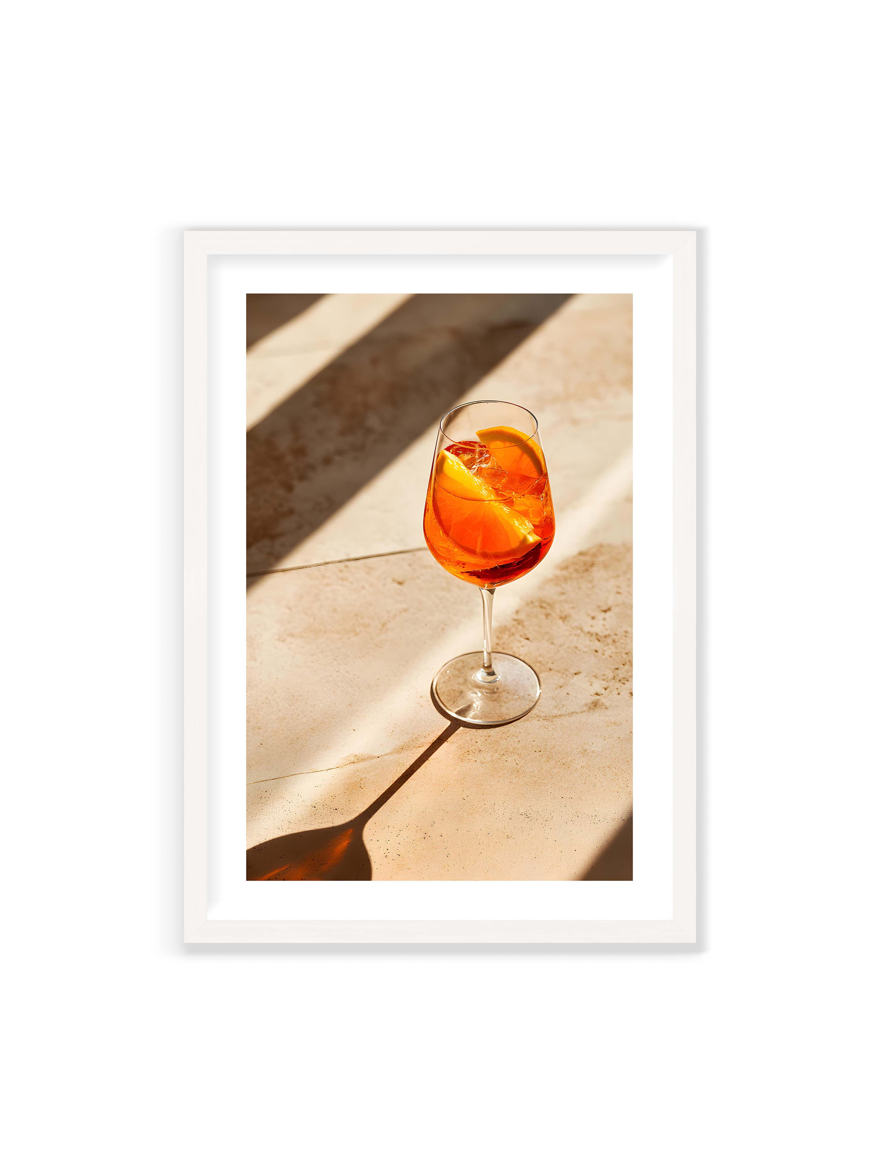 70x100 cm mit weißem Galerie-Rand mit weißem Rahmen – Aperitifglas mit orangefarbenem Drink und Orangenscheiben, Sonnenlicht und langer Schatten auf hellem Stein.