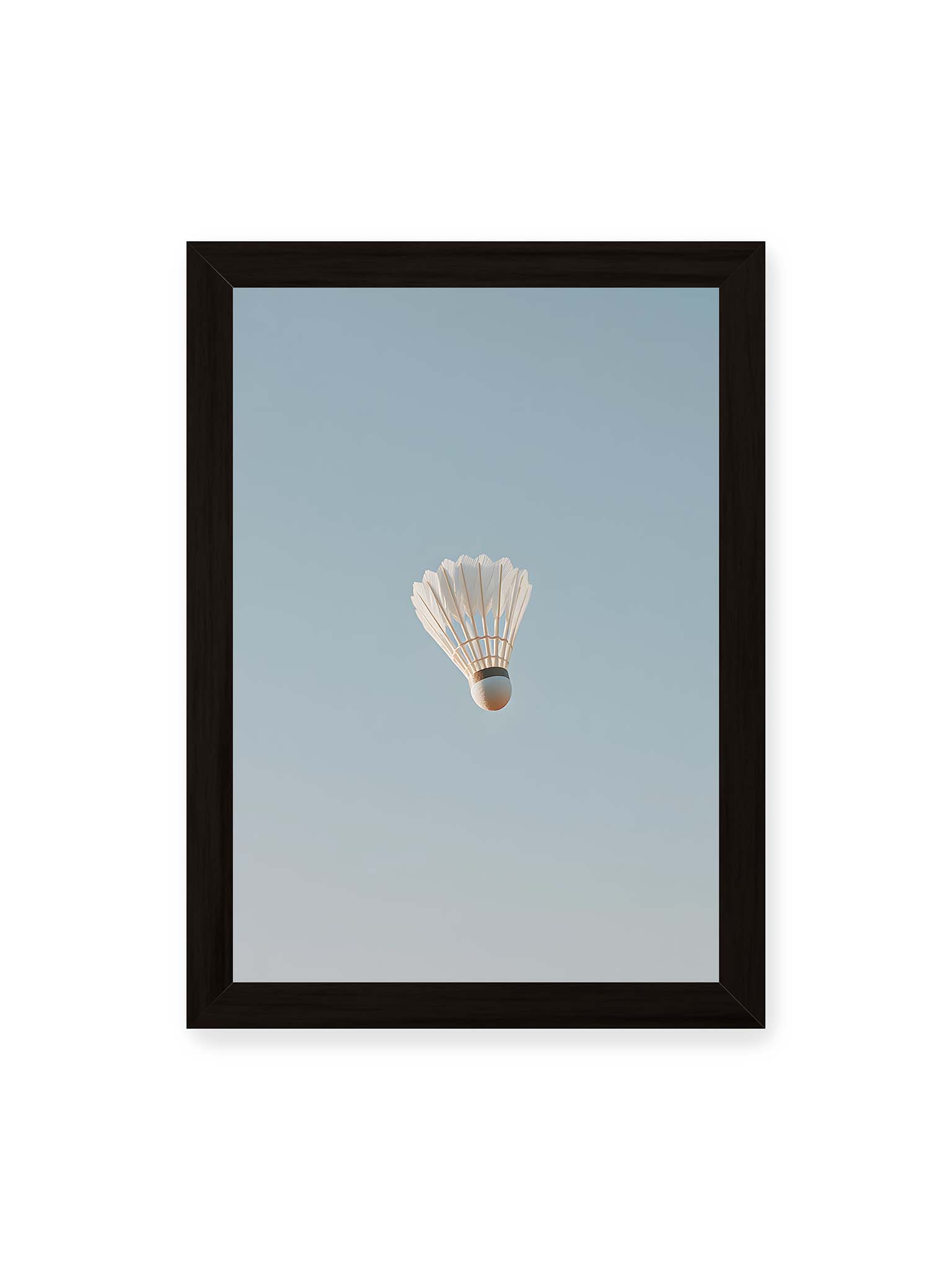 21x30 cm, schwarzer Rahmen – Weißer Federball schwebt zentriert vor hellblauem Himmel, minimalistische Komposition mit viel Freiraum.