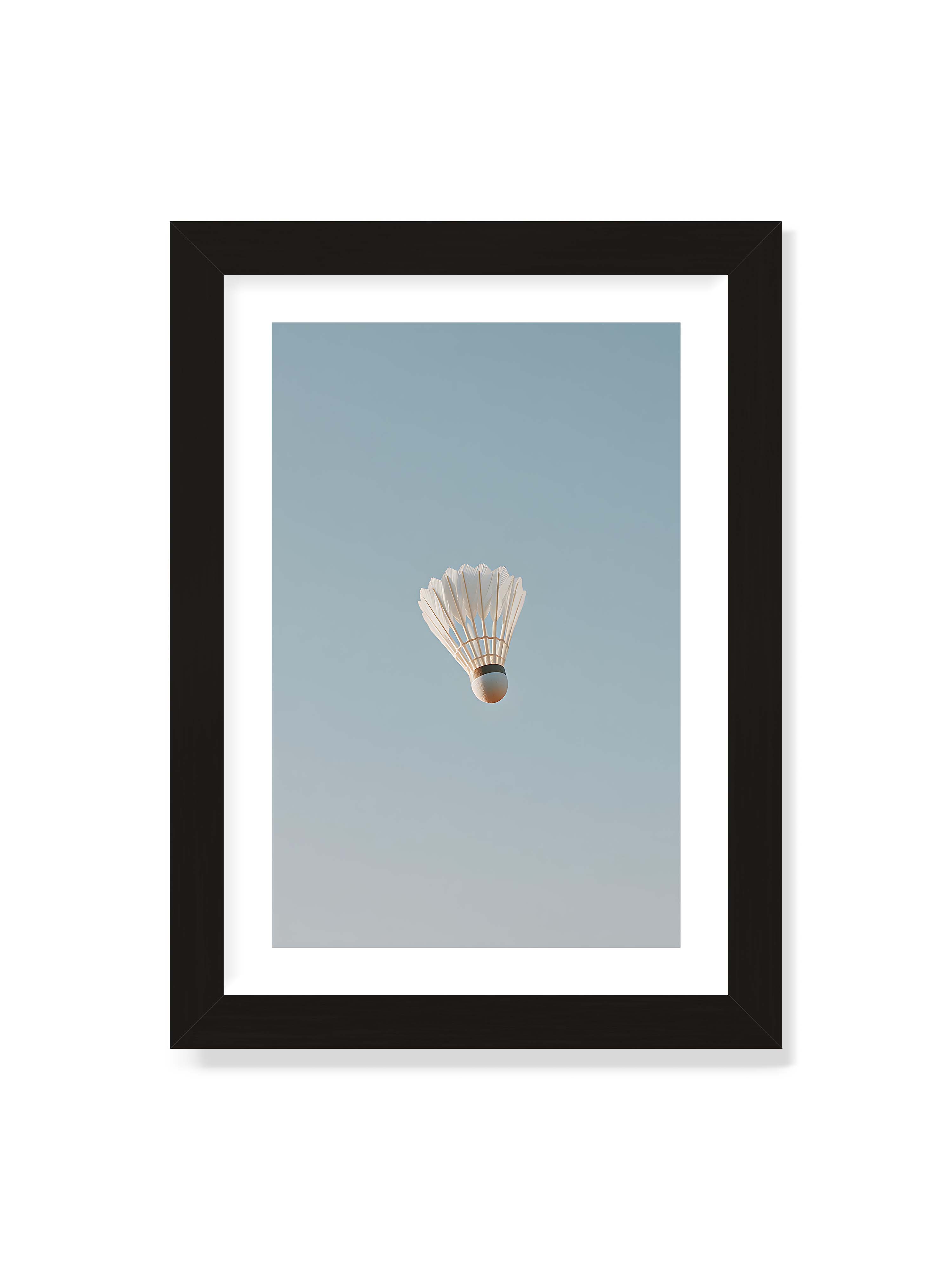 21x30 cm mit weißem Galerie-Rand mit schwarzem Rahmen – Weißer Federball schwebt zentriert vor hellblauem Himmel, minimalistische Komposition mit viel Freiraum.