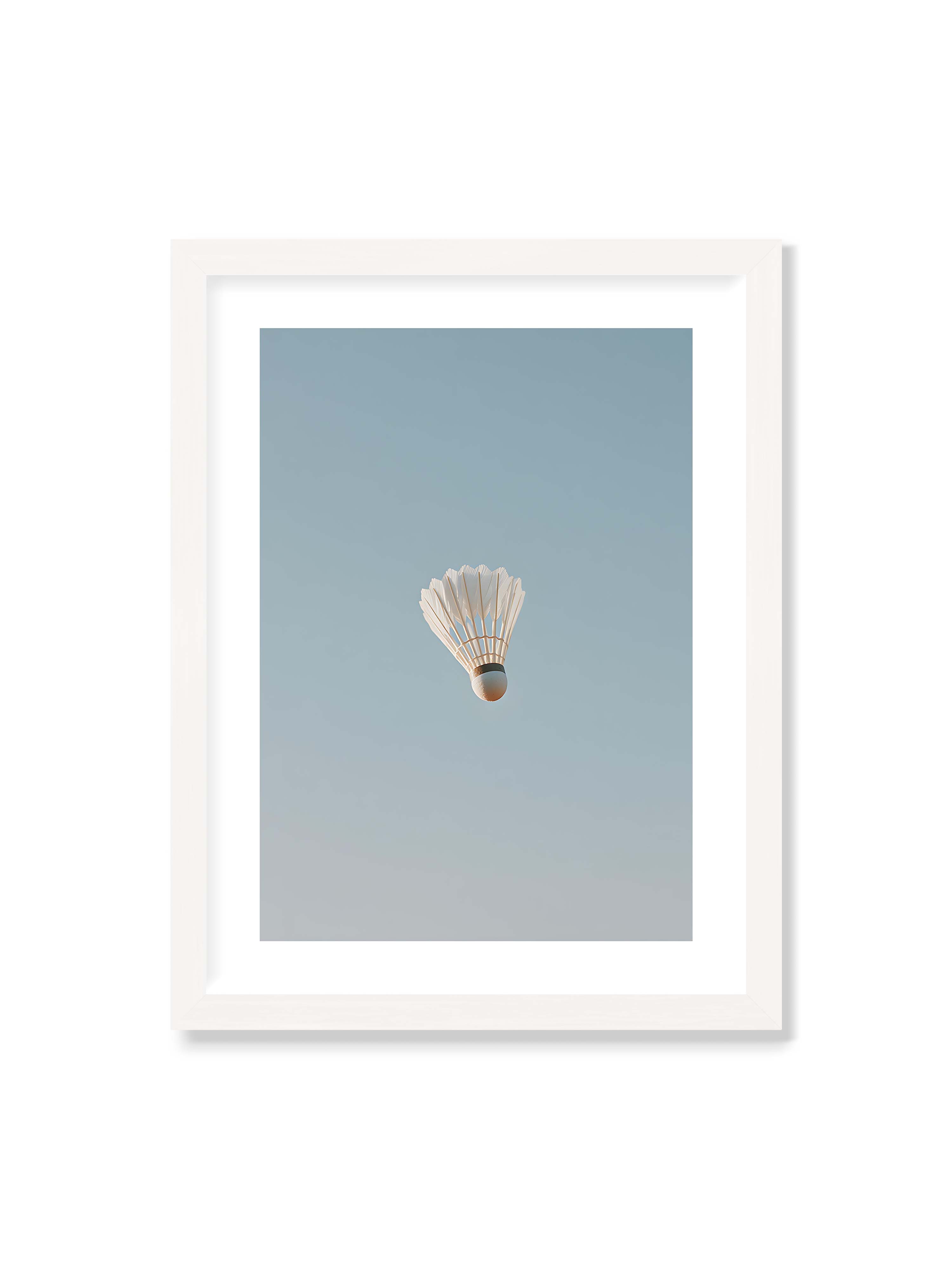 30x40 cm mit weißem Galerie-Rand mit weißem Rahmen – Weißer Federball schwebt zentriert vor hellblauem Himmel, minimalistische Komposition mit viel Freiraum.