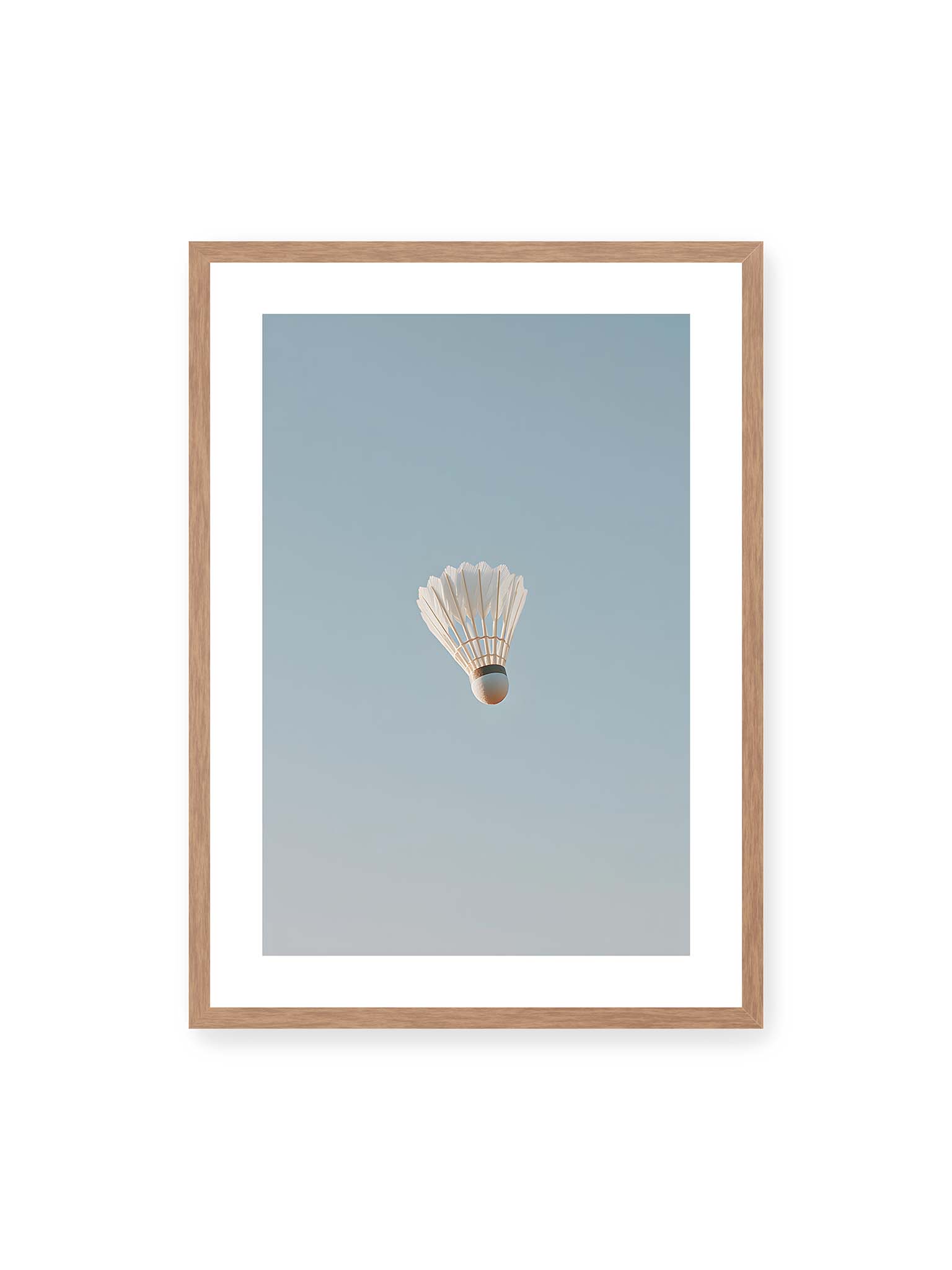 50x70 cm, weißer Galerie-Rand, Eichenrahmen – Weißer Federball schwebt zentriert vor hellblauem Himmel, minimalistische Komposition mit viel Freiraum.