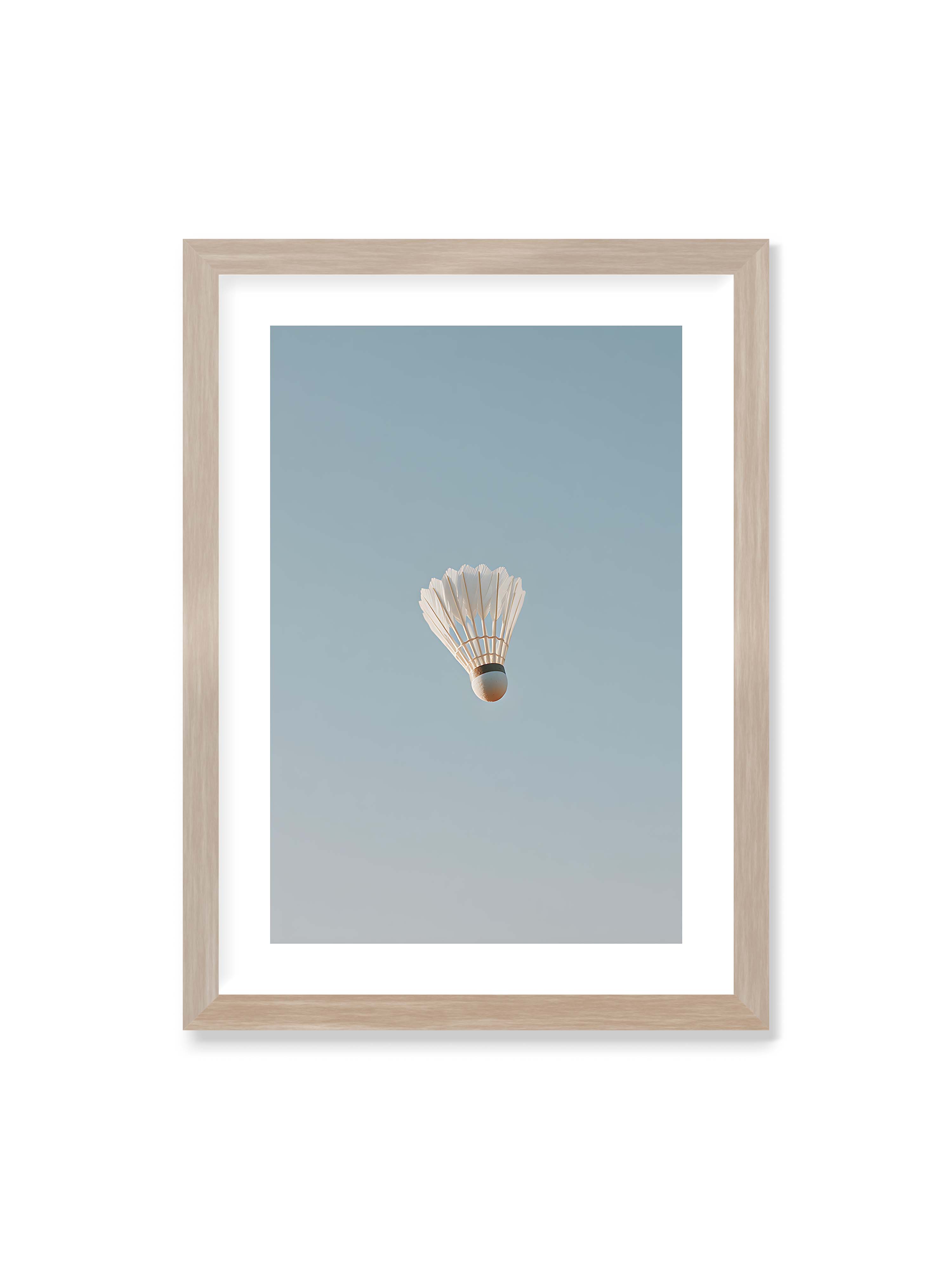 50x70 cm mit weißem Galerie-Rand im Eichenrahmen – Weißer Federball schwebt zentriert vor hellblauem Himmel, minimalistische Komposition mit viel Freiraum.