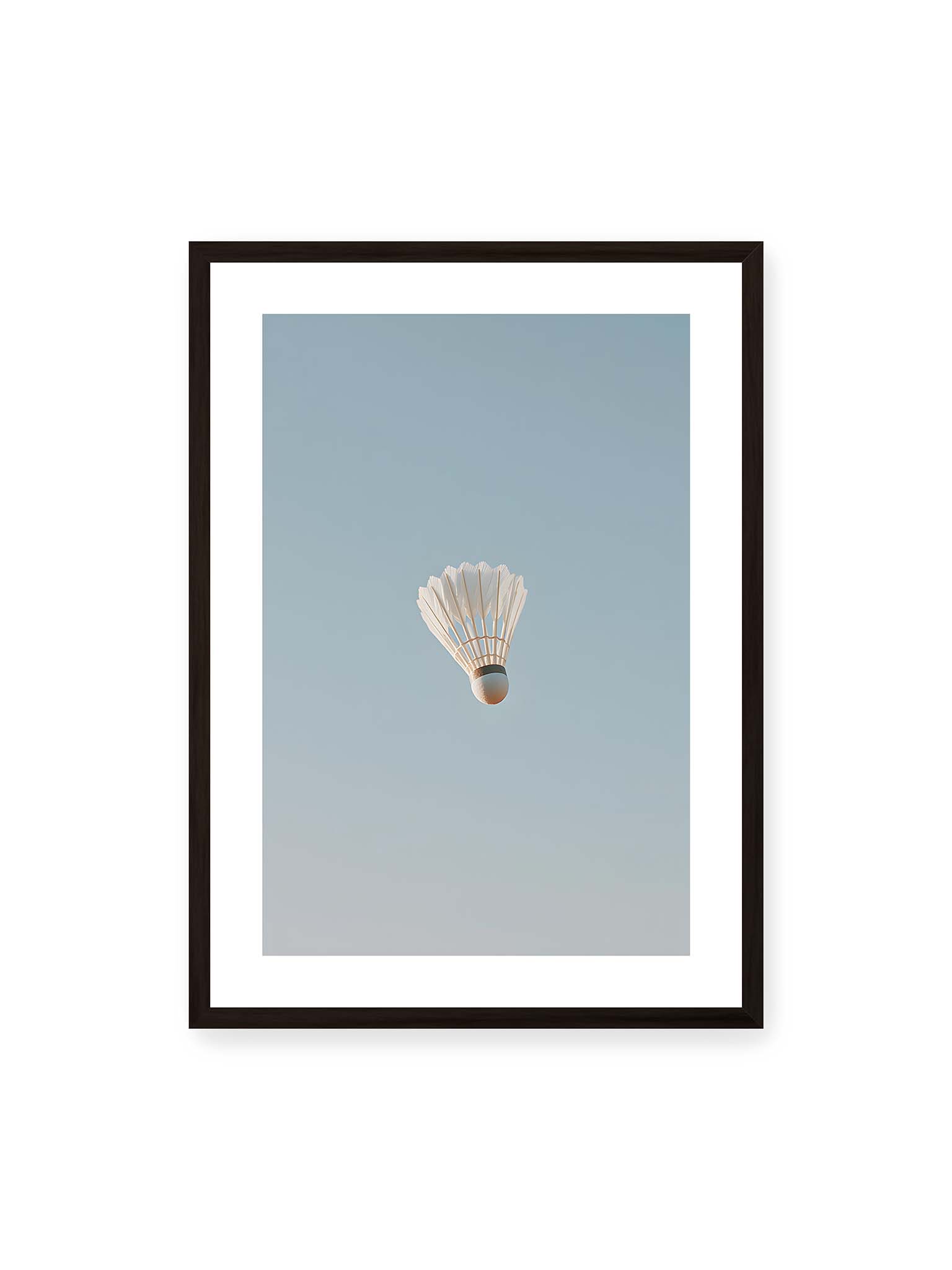50x70 cm, weißer Galerie-Rand, schwarzer Rahmen – Weißer Federball schwebt zentriert vor hellblauem Himmel, minimalistische Komposition mit viel Freiraum.