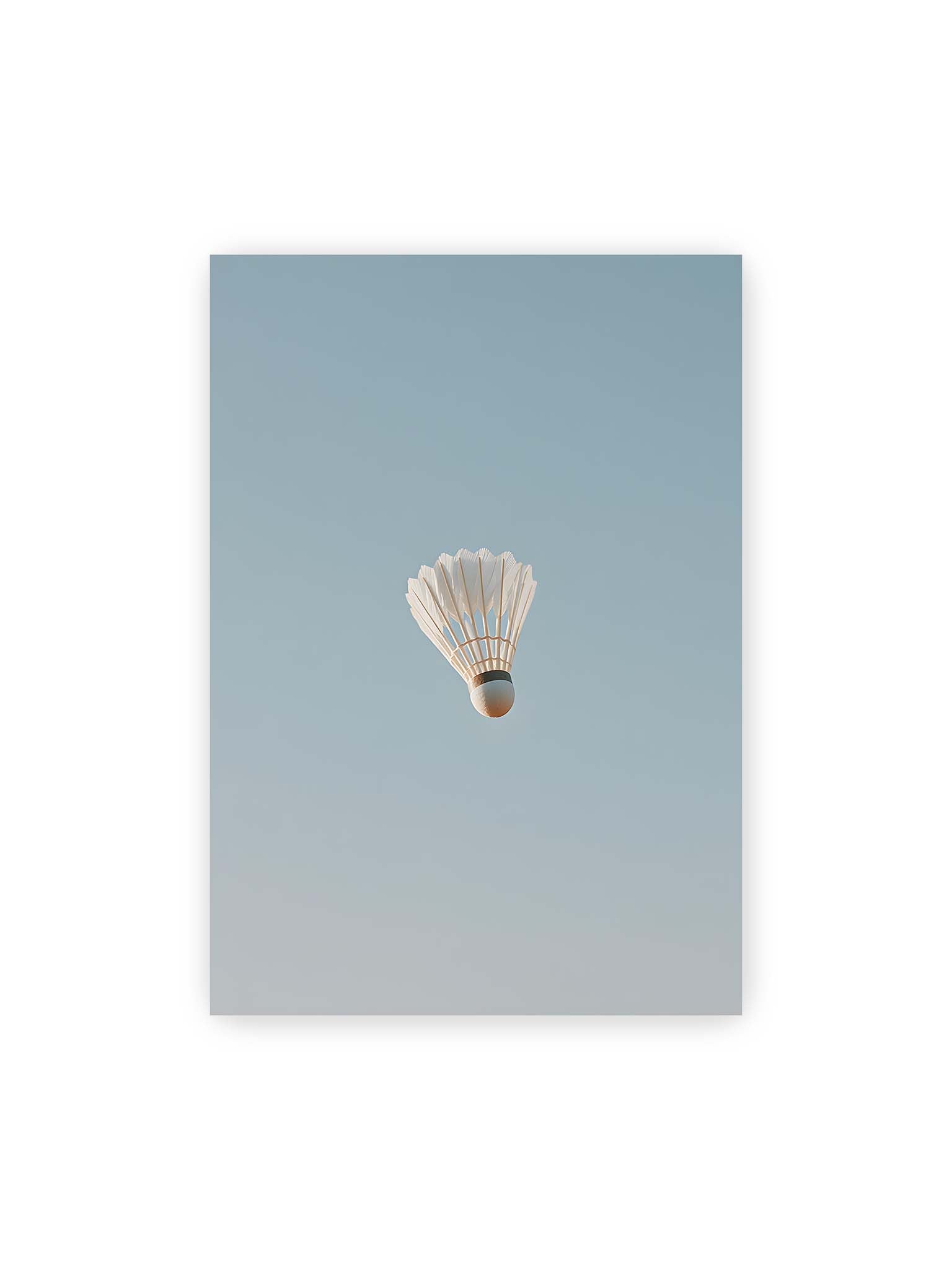 70x100 cm – Weißer Federball schwebt zentriert vor hellblauem Himmel, minimalistische Komposition mit viel Freiraum.