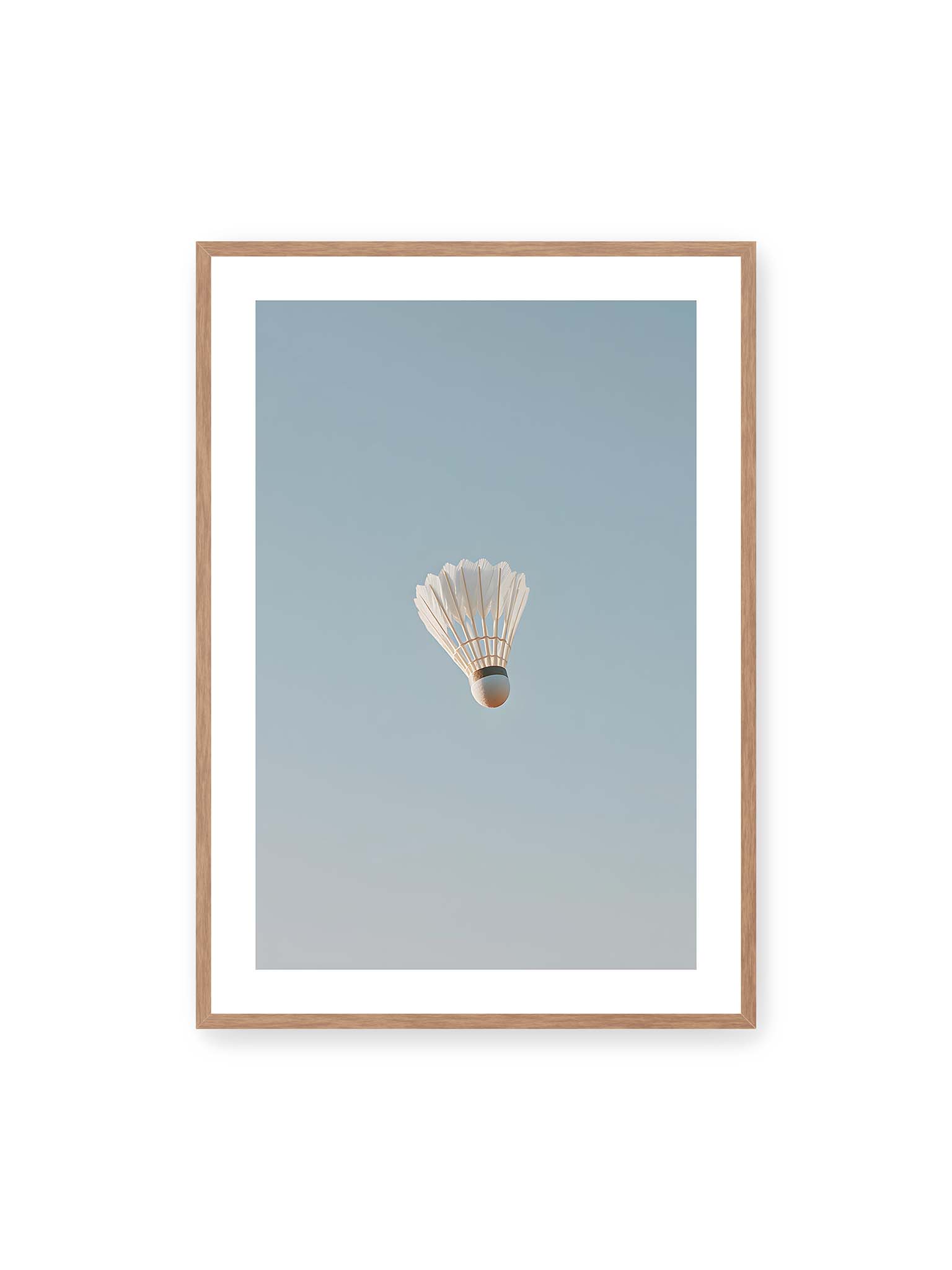 70x100 cm, weißer Galerie-Rand, Eichenrahmen – Weißer Federball schwebt zentriert vor hellblauem Himmel, minimalistische Komposition mit viel Freiraum.