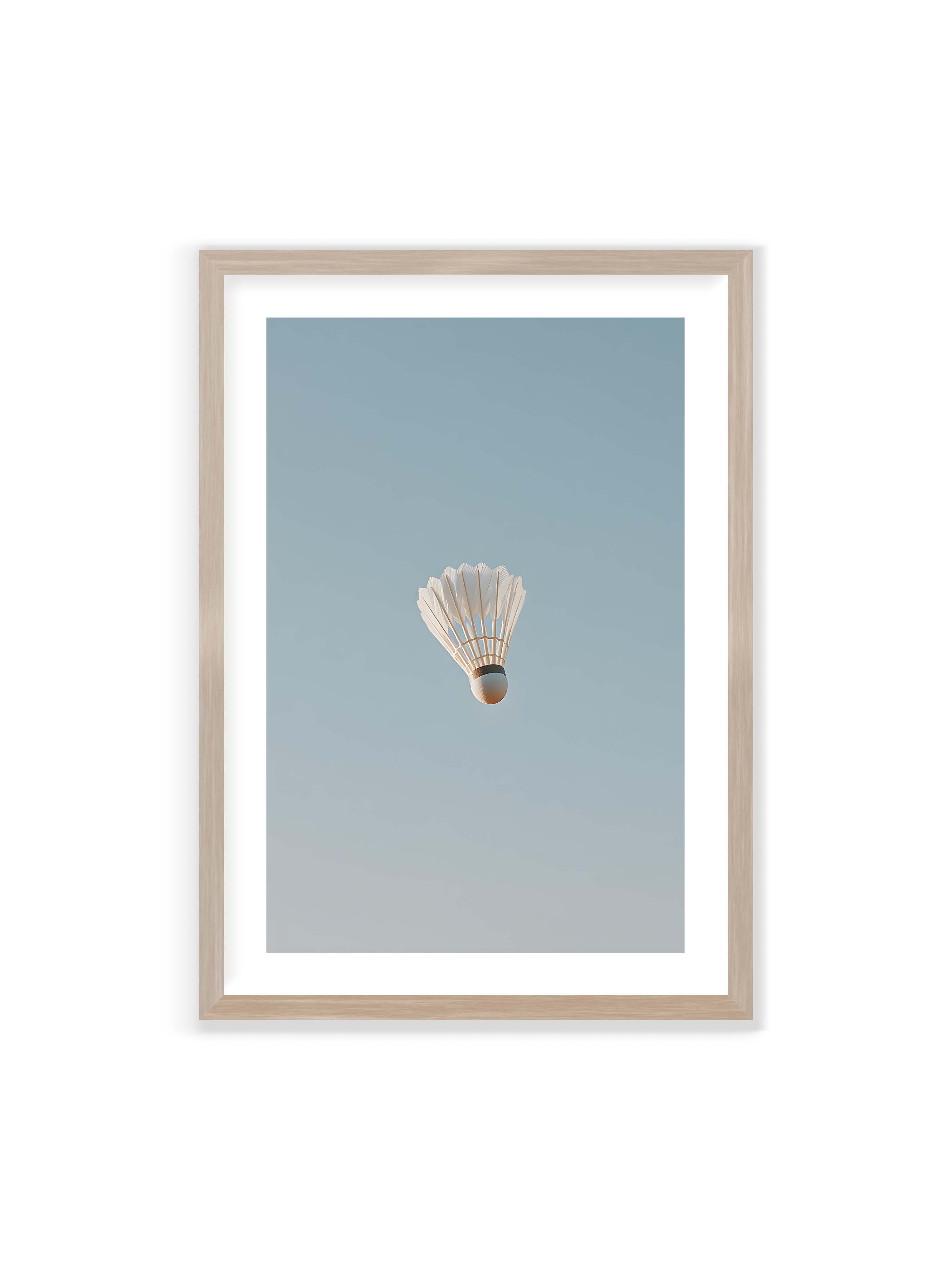 70x100 cm mit weißem Galerie-Rand im Eichenrahmen – Weißer Federball schwebt zentriert vor hellblauem Himmel, minimalistische Komposition mit viel Freiraum.