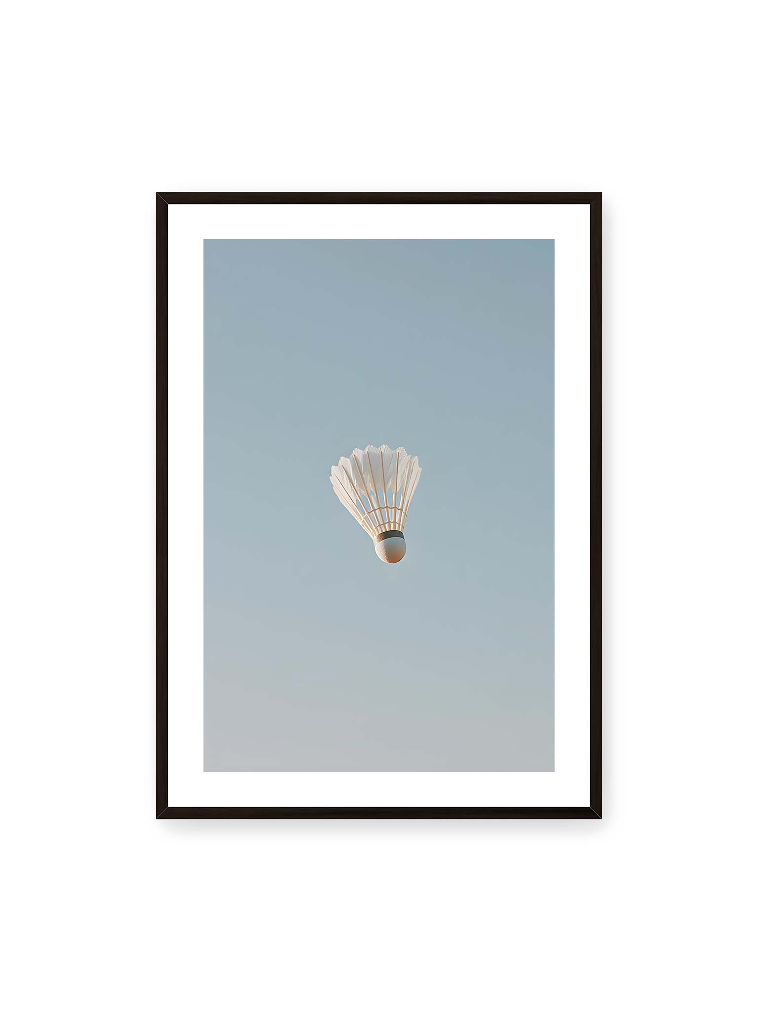 70x100 cm, weißer Galerie-Rand, schwarzer Rahmen – Weißer Federball schwebt zentriert vor hellblauem Himmel, minimalistische Komposition mit viel Freiraum.