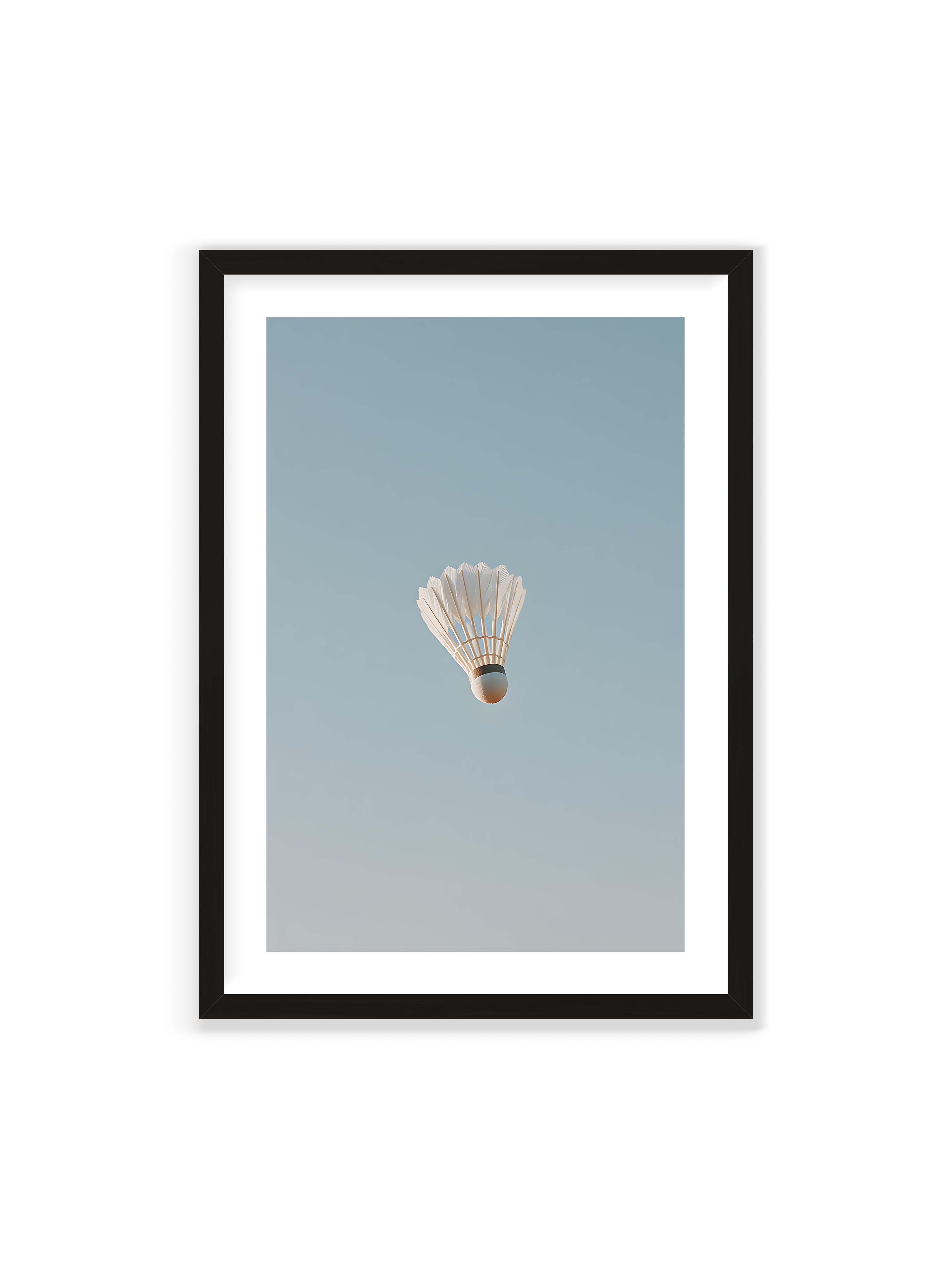 70x100 cm mit weißem Galerie-Rand mit schwarzem Rahmen – Weißer Federball schwebt zentriert vor hellblauem Himmel, minimalistische Komposition mit viel Freiraum.