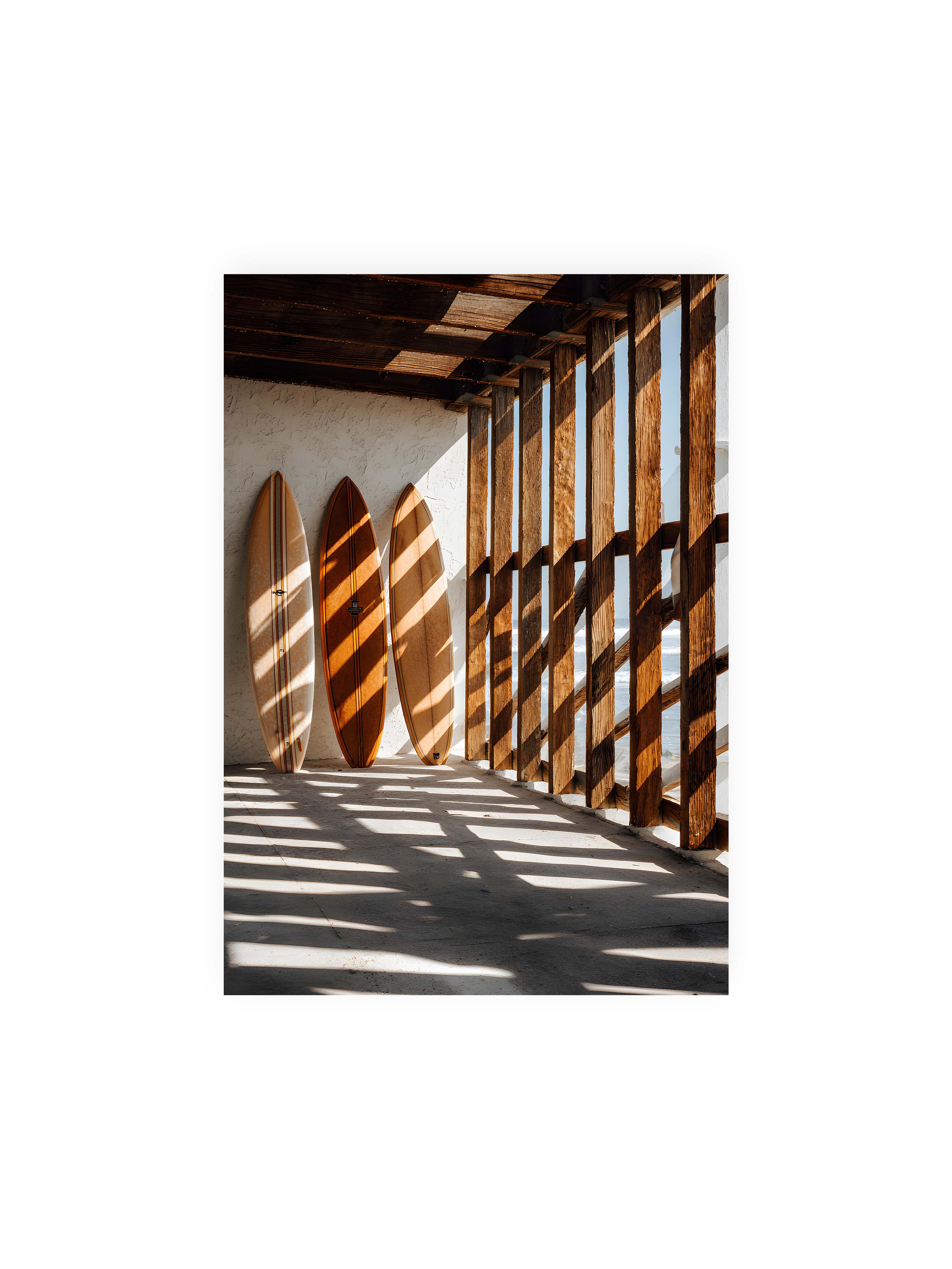 21x30 cm ohne Galerie-Rand ohne Rahmen – Drei Surfboards an einer hellen Wand, Holzpfosten werfen diagonale Schatten; Meer und Himmel schimmern im Hintergrund.