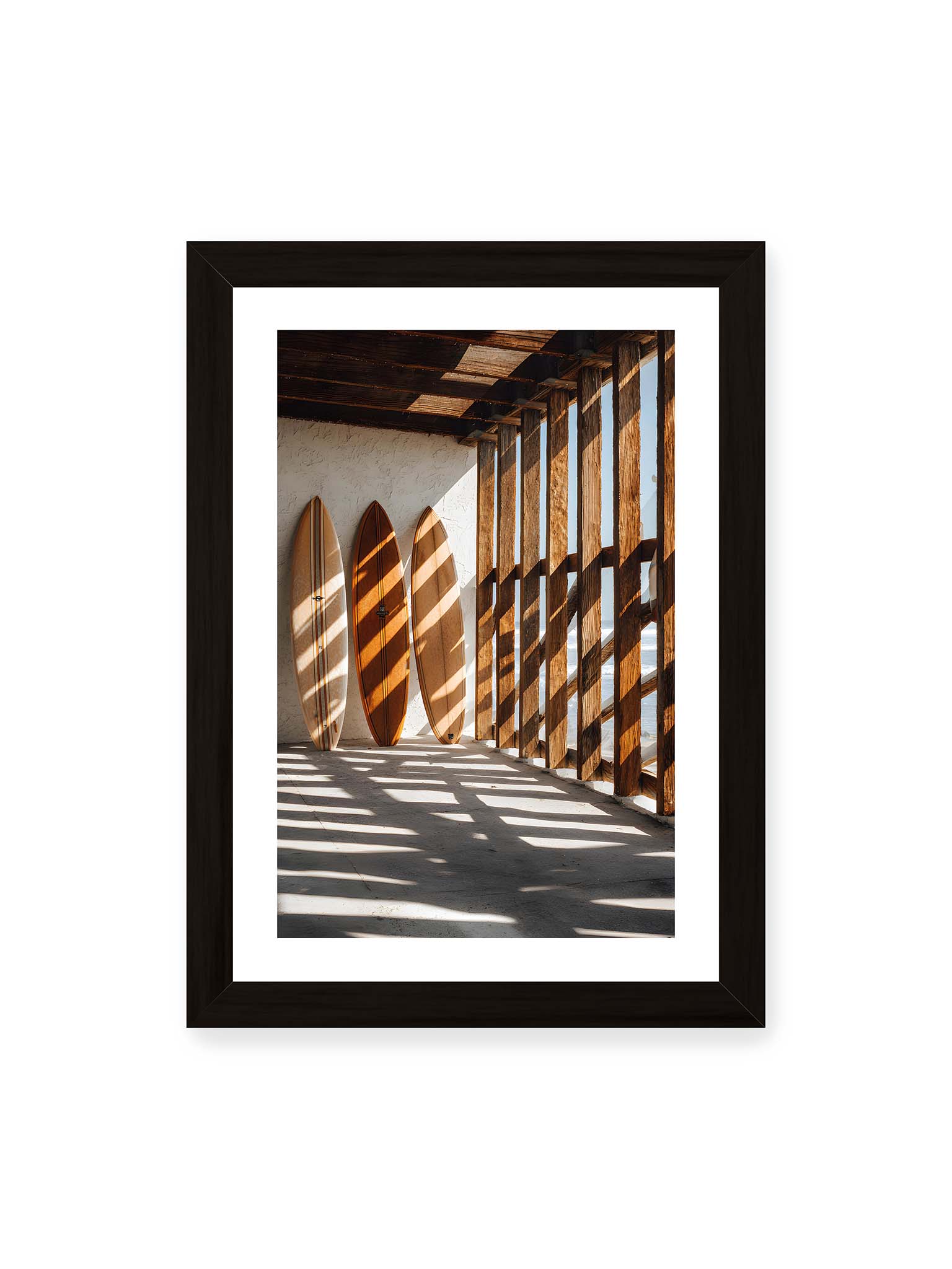 21x30 cm, weißer Galerie-Rand, schwarzer Rahmen – Drei Surfboards an einer hellen Wand, Holzpfosten werfen diagonale Schatten; Meer und Himmel schimmern im Hintergrund.