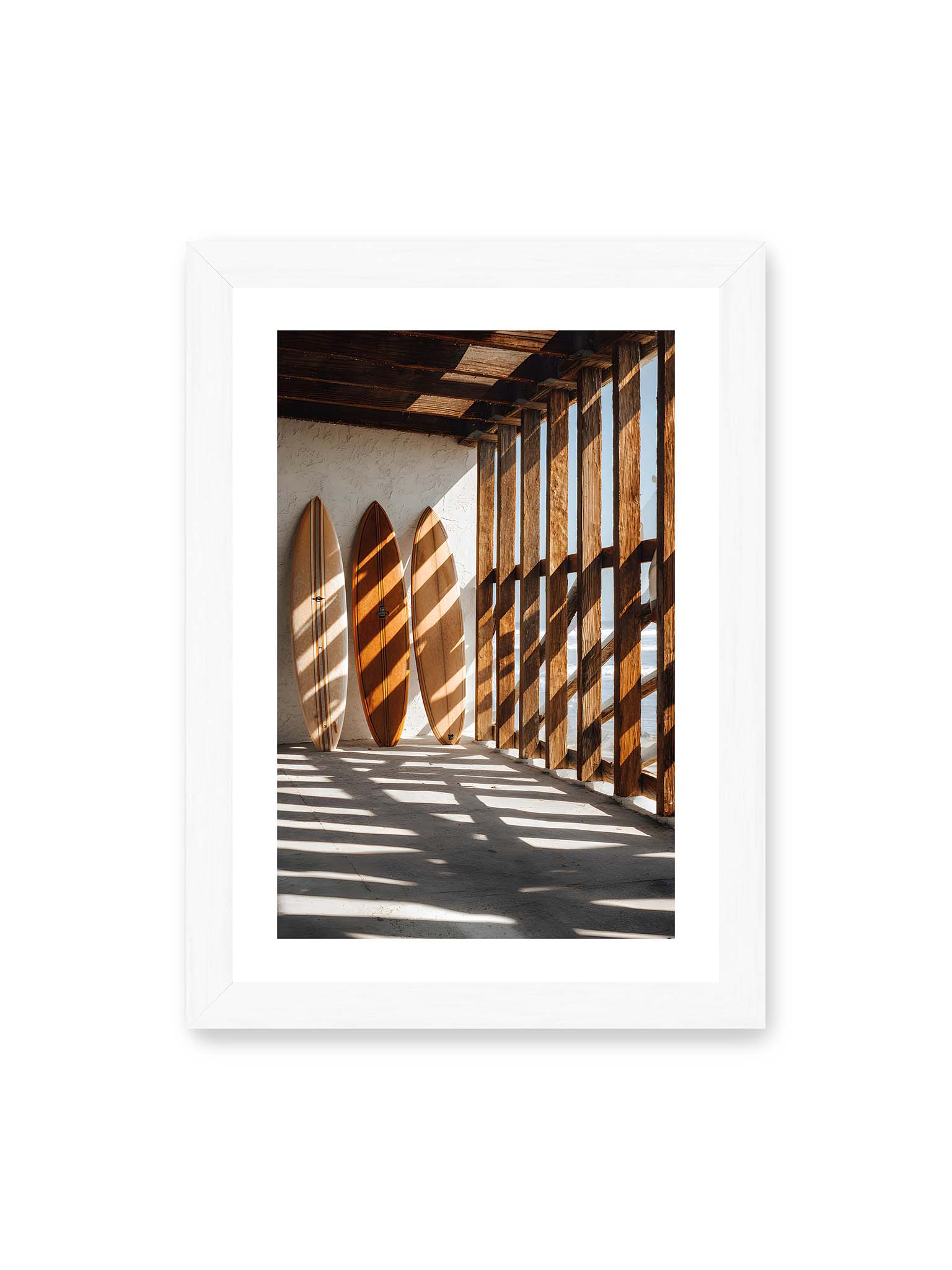 21x30 cm, weißer Galerie-Rand, weißer Rahmen – Drei Surfboards an einer hellen Wand, Holzpfosten werfen diagonale Schatten; Meer und Himmel schimmern im Hintergrund.